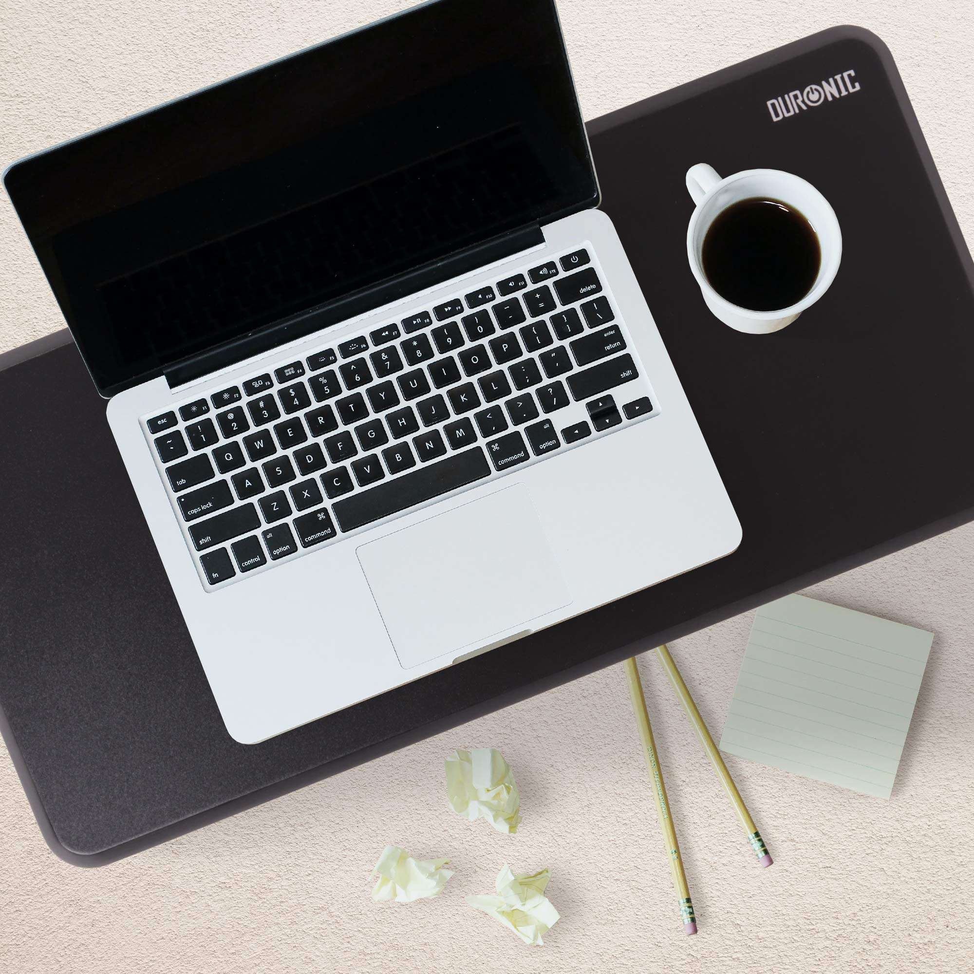Laptop, Tasse und Schreibwaren auf schwarzem Schreibtischpad.