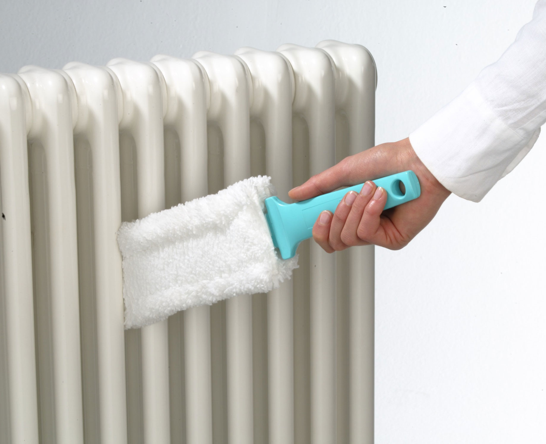 Una mano limpiando un radiador blanco con un plumero de mango azul.