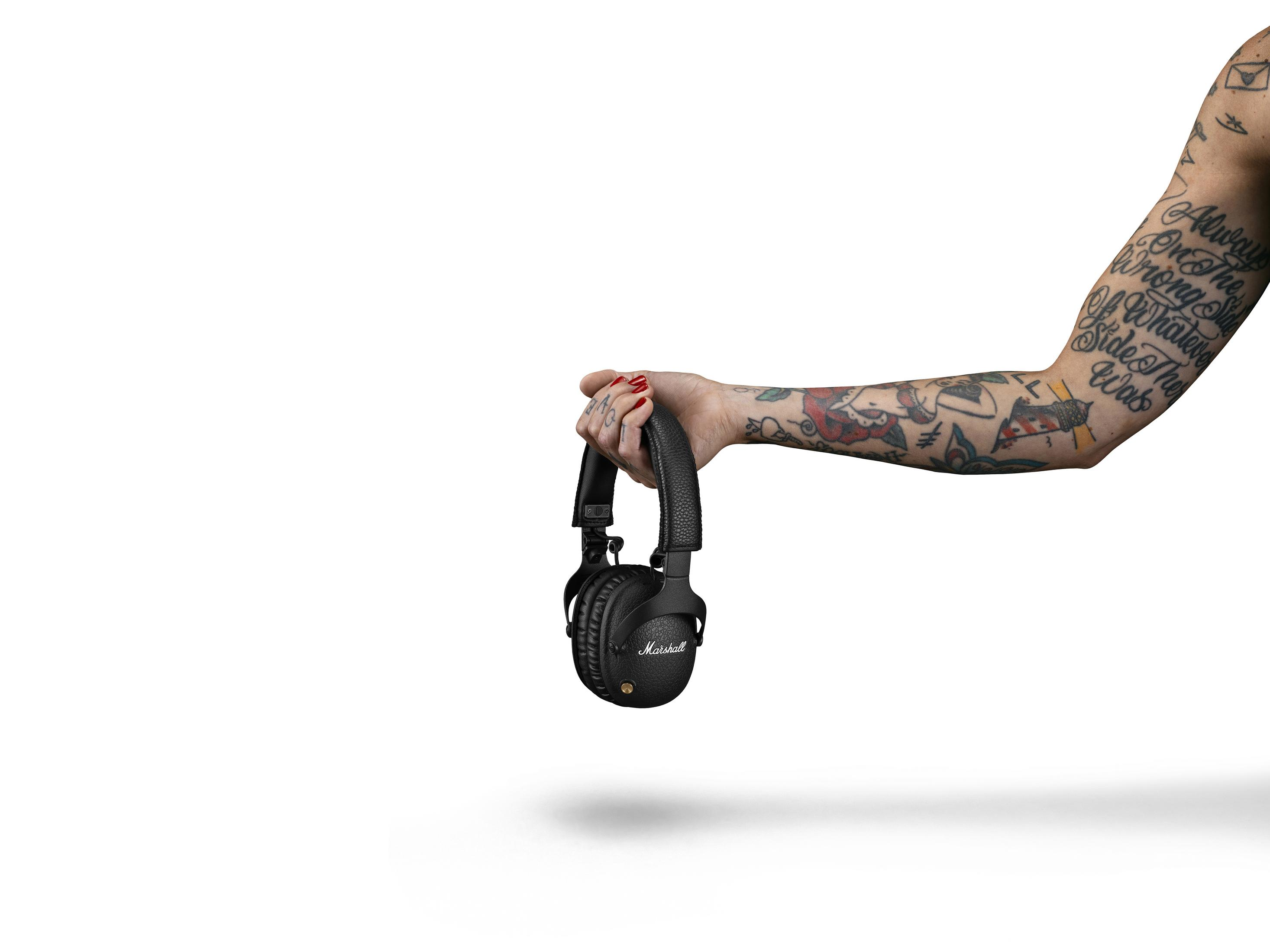 Persona sosteniendo auriculares Marshall negros, tatuajes visibles.