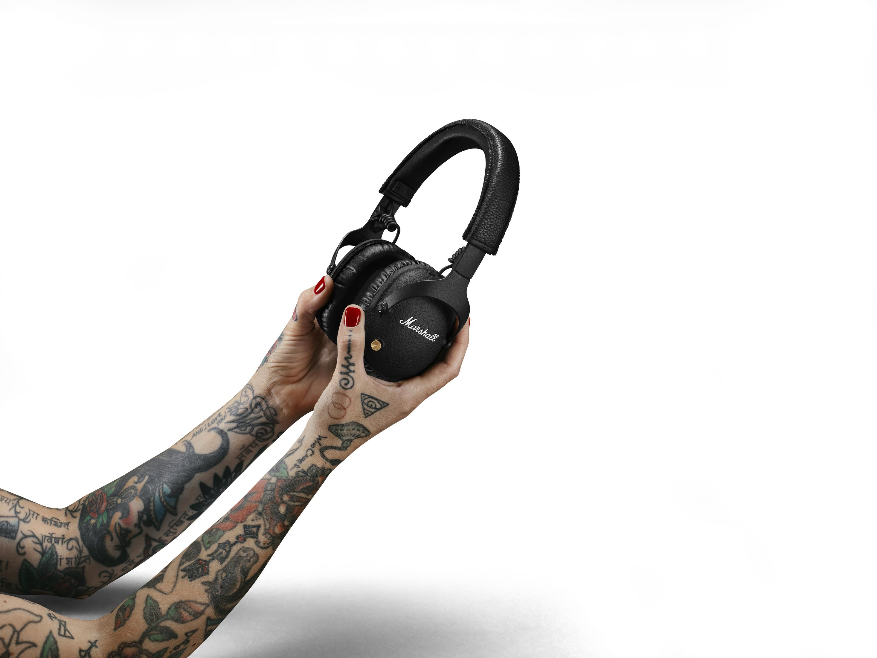 Manos tatuadas sosteniendo auriculares Marshall negros sobre fondo blanco.