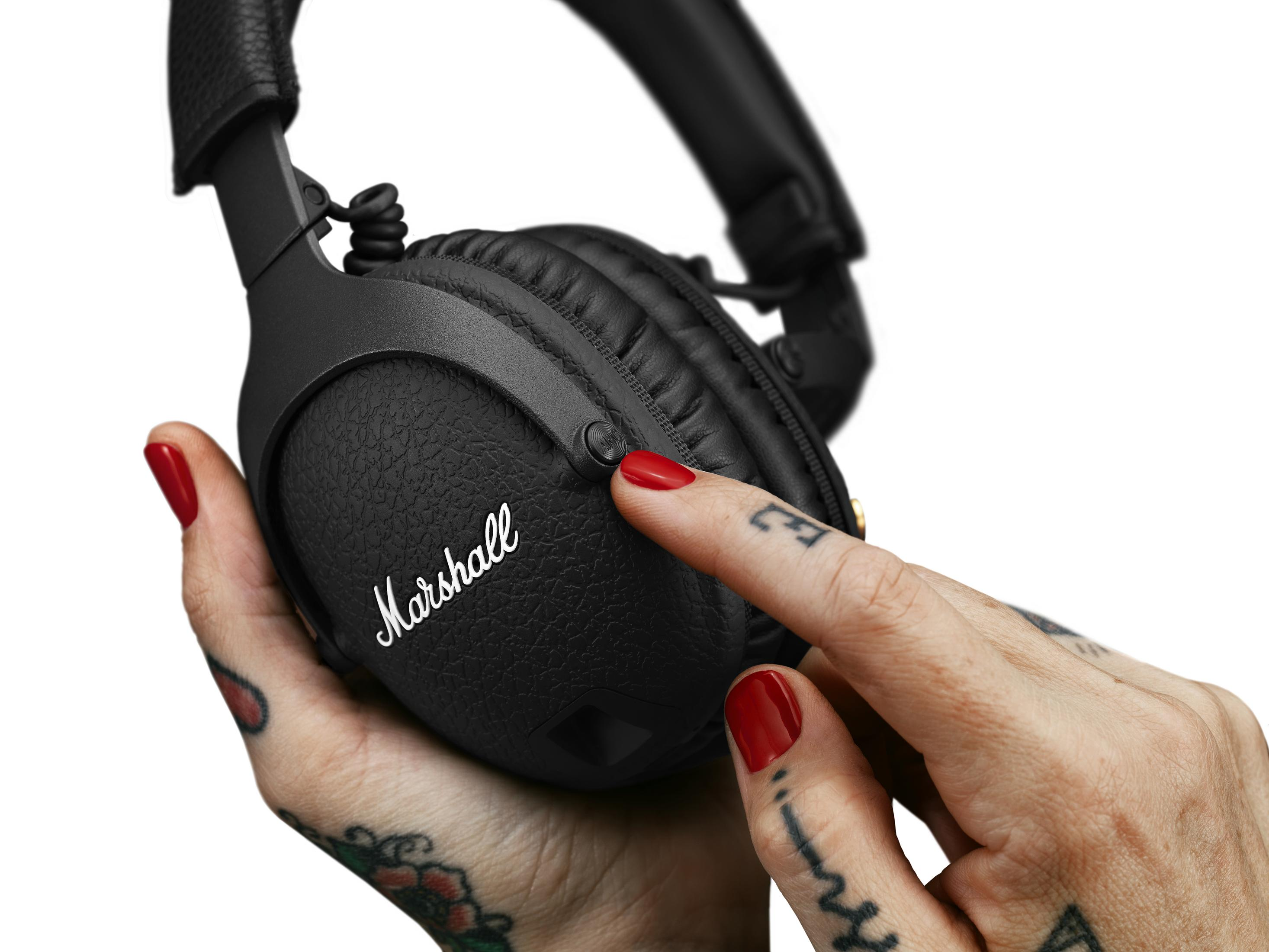 Auriculares Marshall negros. Una mano con esmalte rojo presiona el botón de encendido.