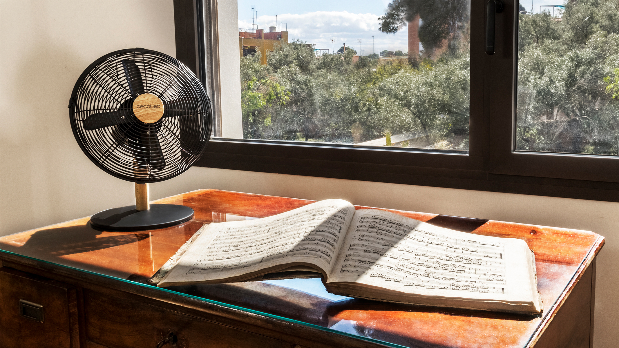 Czarny i drewniany wentylator na stole z otwartymi nutami i oknem w tle.