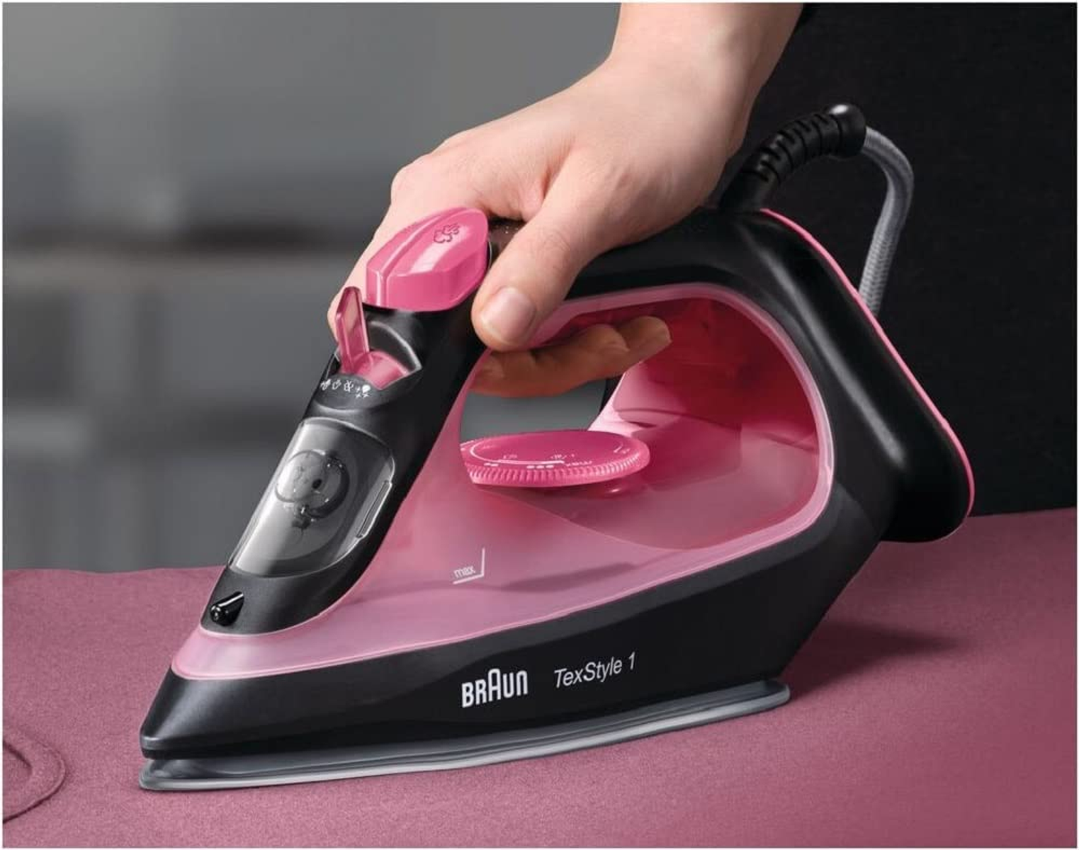 Una persona che stira con un ferro nero e rosa su un tessuto rosa.