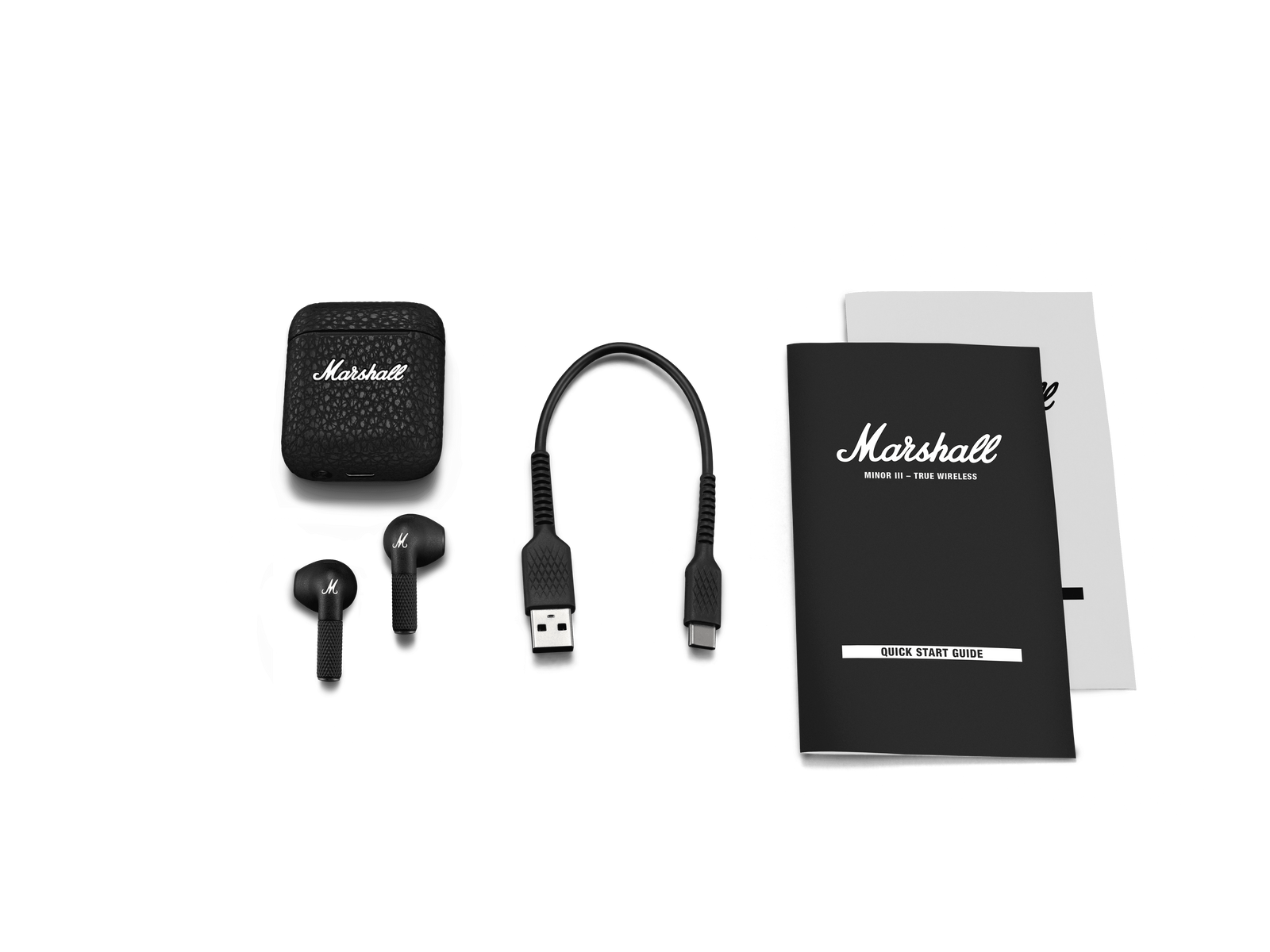 Estuche negro, auriculares, cable de carga y documentos sobre una superficie negra.