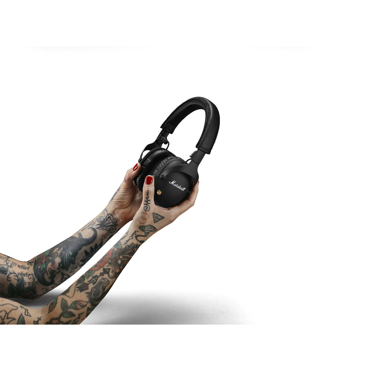 Mujer sosteniendo auriculares Marshall negros. Tatuajes visibles, sobre fondo blanco.