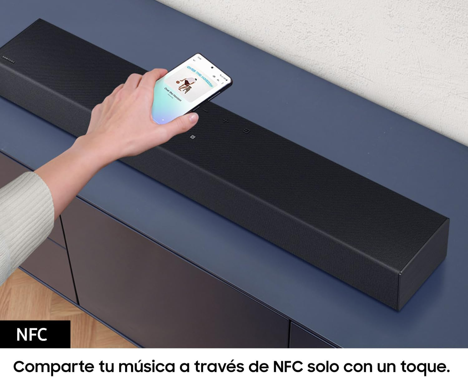 Dłoń dotykająca soundbara z telefonem wyświetlającym aplikację muzyczną.