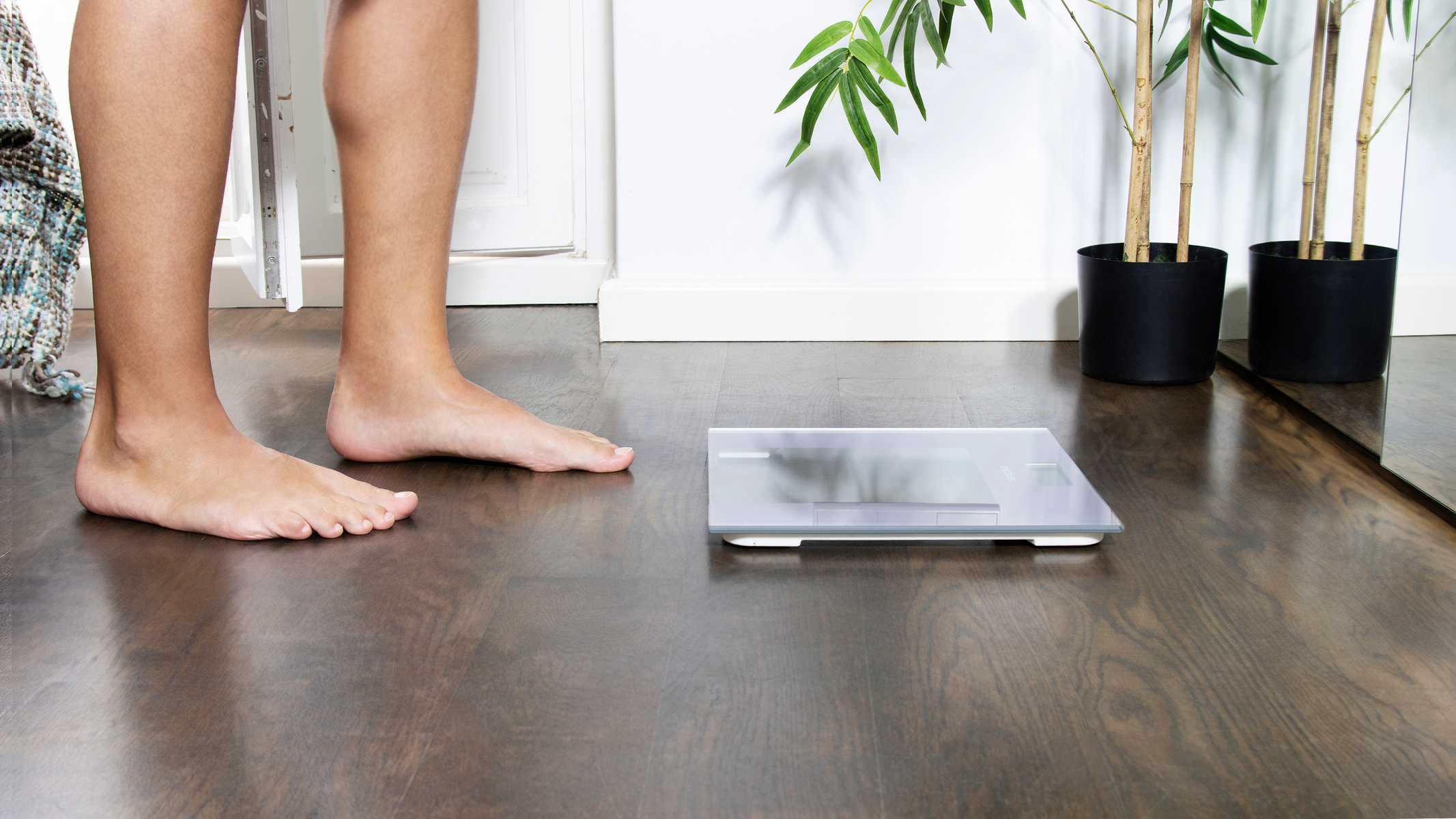 Bose stopy stojące na ciemnej drewnianej podłodze obok wagi cyfrowej.
