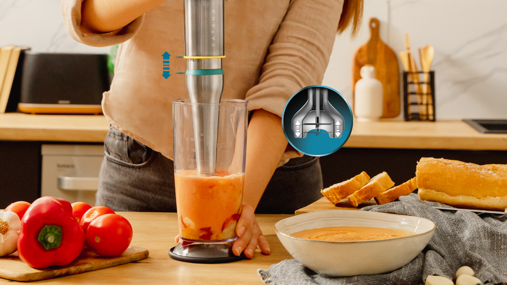 Kobieta blenduje zupę pomidorową blenderem ręcznym. Składniki i chleb obok.