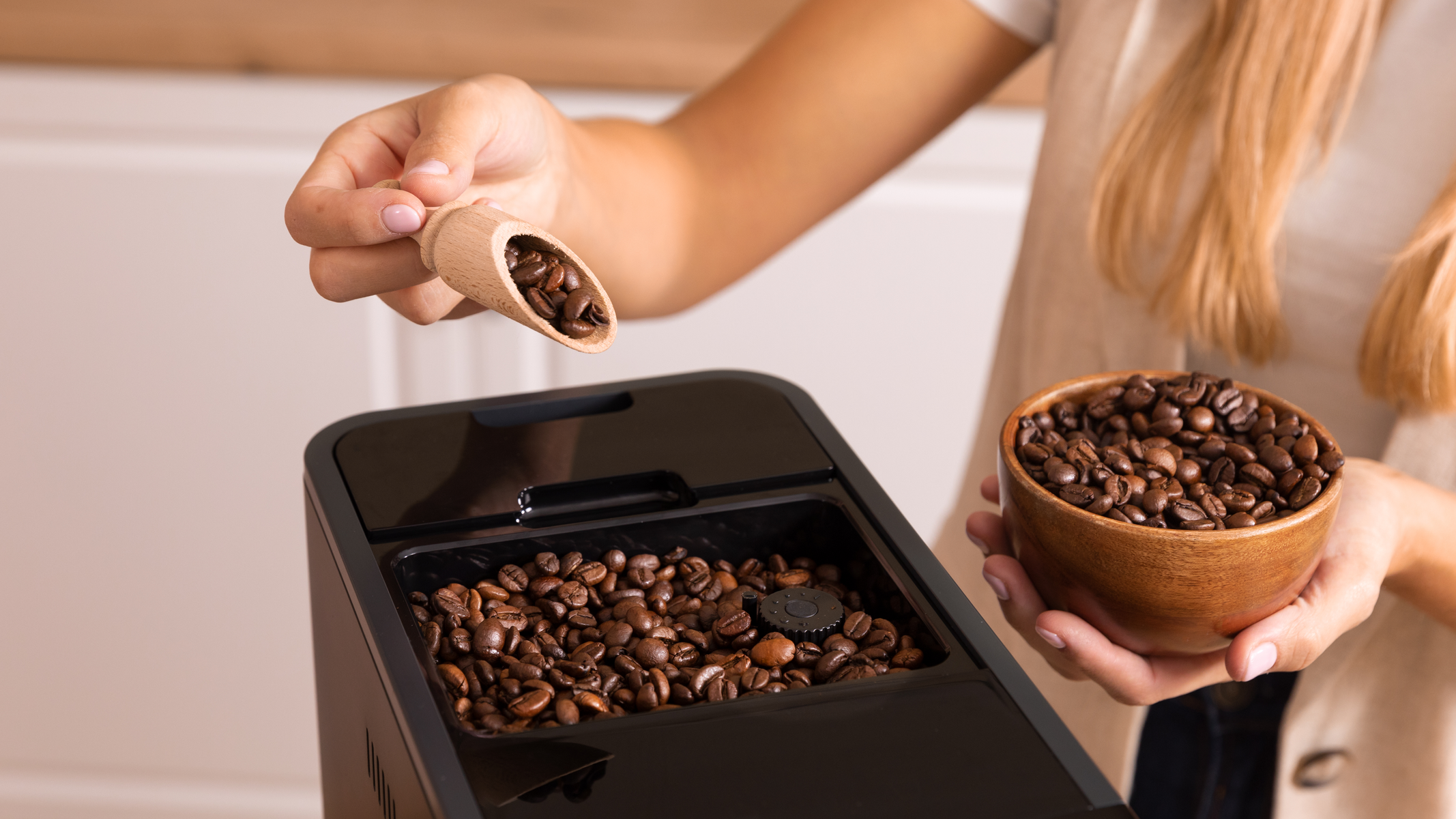 Eine Person schüttet Kaffeebohnen aus einem Holzschöpfer in eine Kaffeemaschine.
