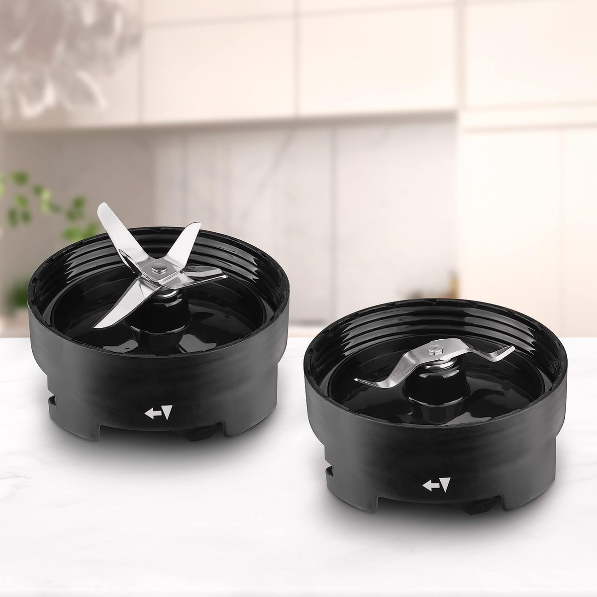 Dwa czarne mocowania ostrzy blendera. Strzałki wskazują kierunek. Na białym blacie.