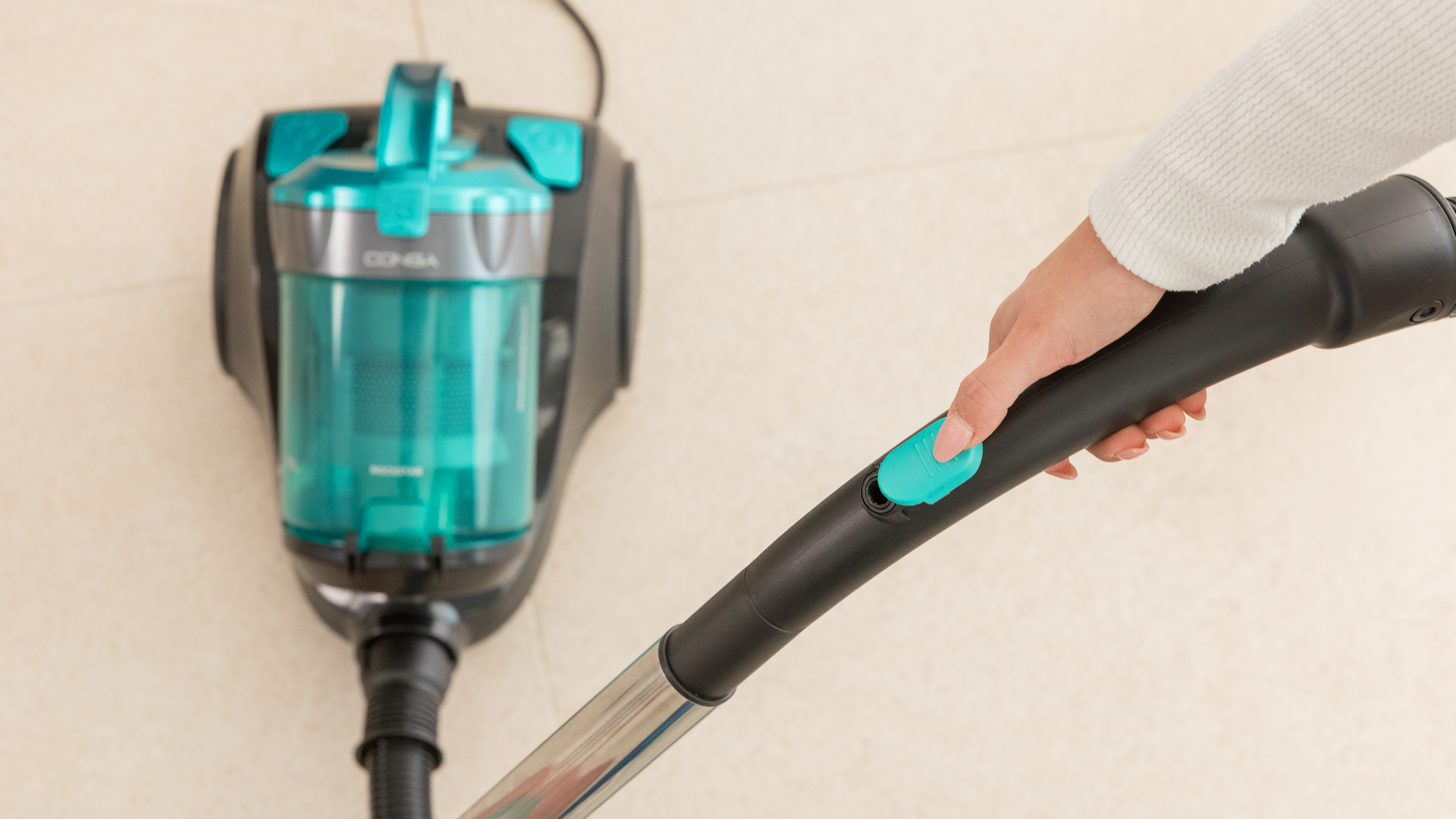 Ręka używająca odkurzacza. Odkurzacz jest turkusowy i czarny.
