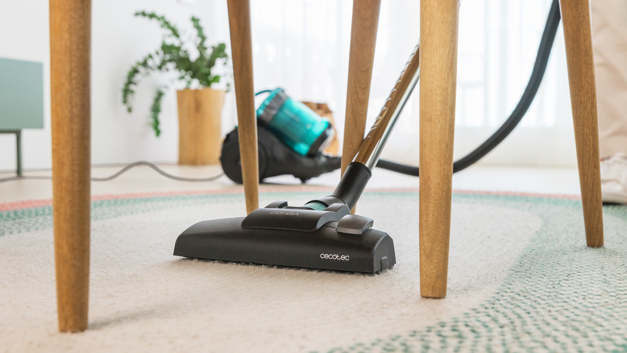 Głowica odkurzacza pod stołem z drewnianymi nogami, na dywanie z okrągłym wzorem, w pokoju.