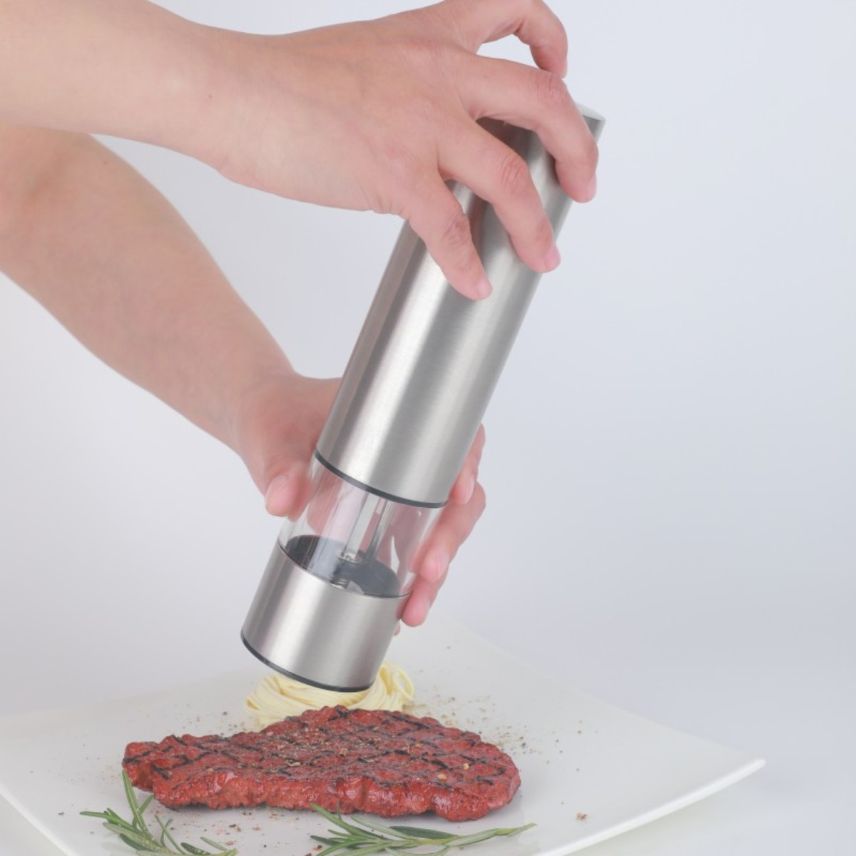 Mano usando un molinillo de pimienta de acero inoxidable sobre un plato con comida.