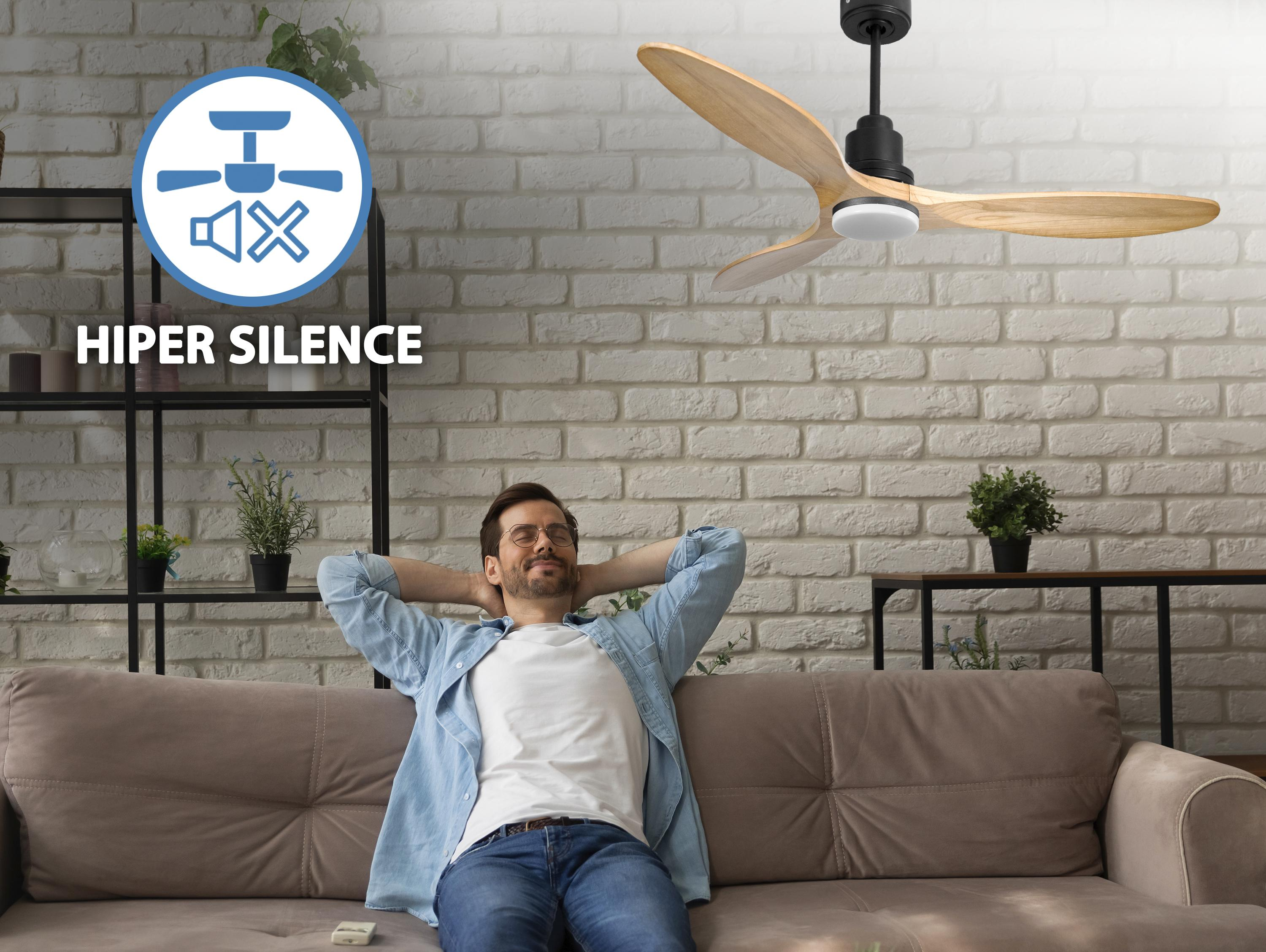 Un hombre relajándose en un sofá con un ventilador de techo arriba. El ventilador es color madera.