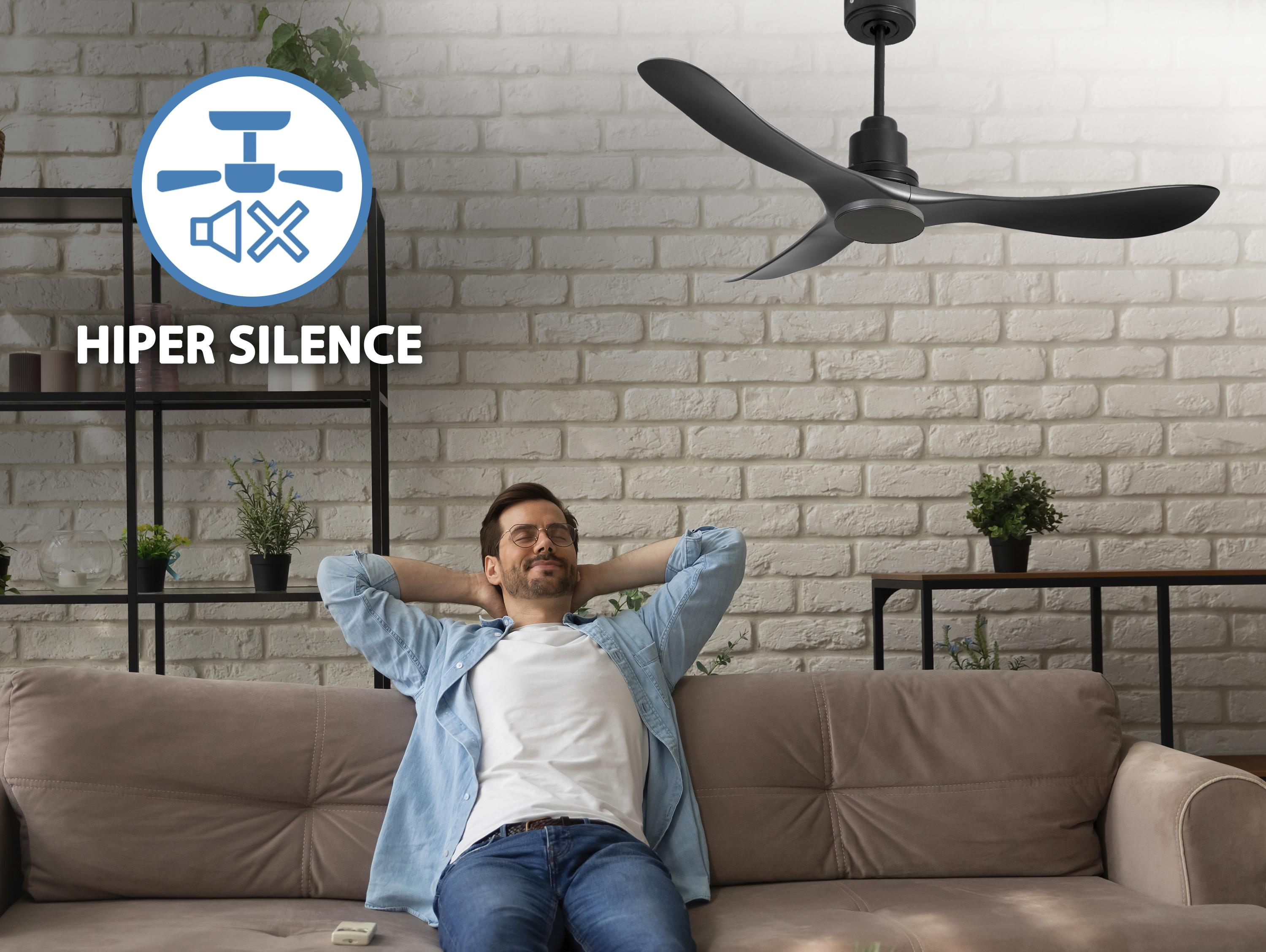 Hombre se relaja bajo un ventilador de techo oscuro. Fondo de pared de ladrillo. El ventilador tiene un motor negro.