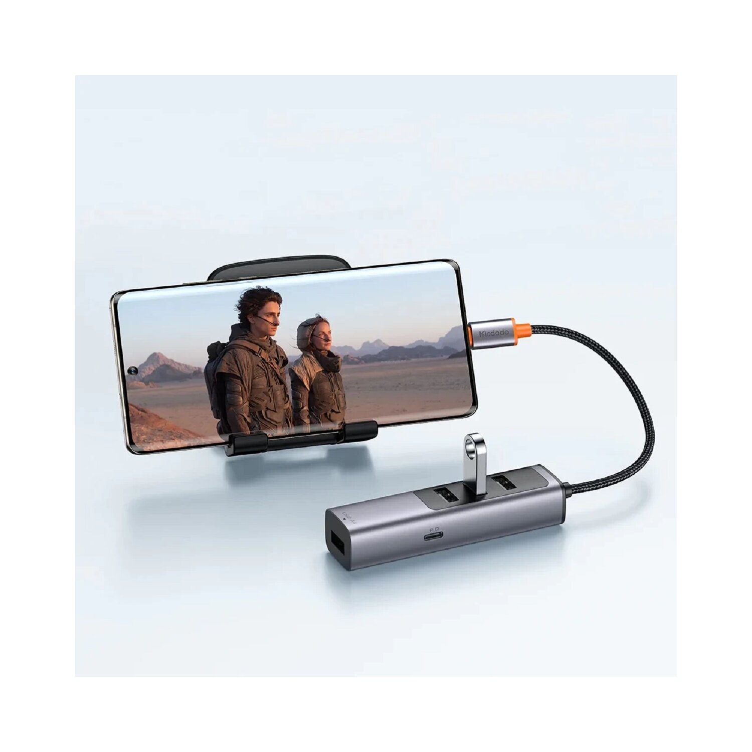 Ein Telefon mit einem Film, der abgespielt wird, gehalten von einem Telefonhalter, verbunden mit einem USB-Hub mit Kabel.