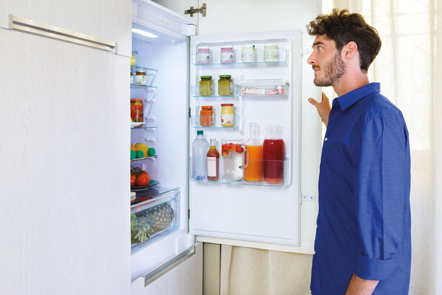 Un uomo guarda un frigorifero pieno di generi alimentari. La porta del frigorifero è aperta.