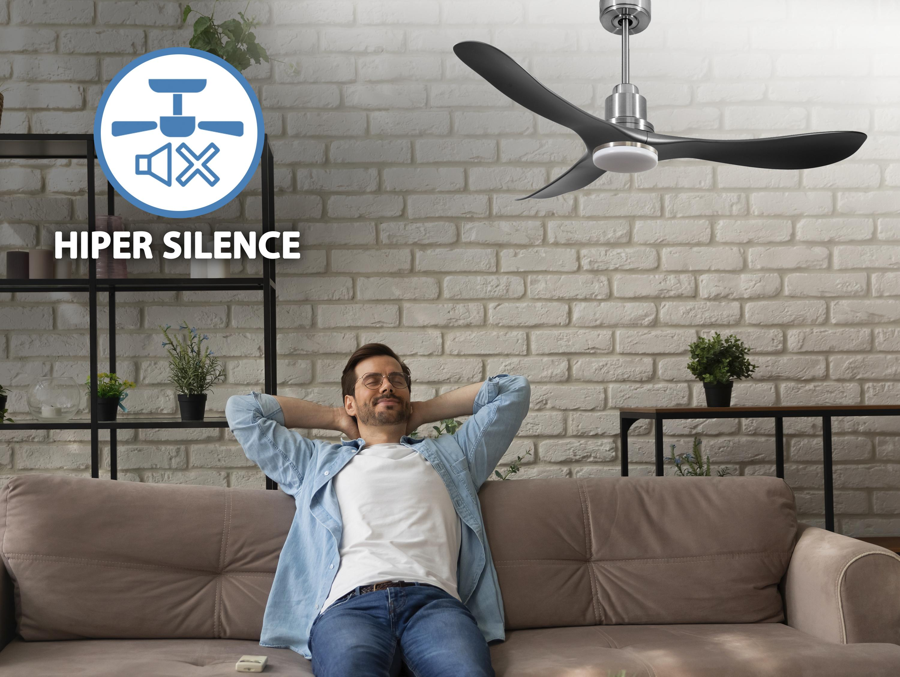 Hombre relajándose en un sofá debajo de un ventilador de techo con aspas oscuras. Texto Hiper Silence.