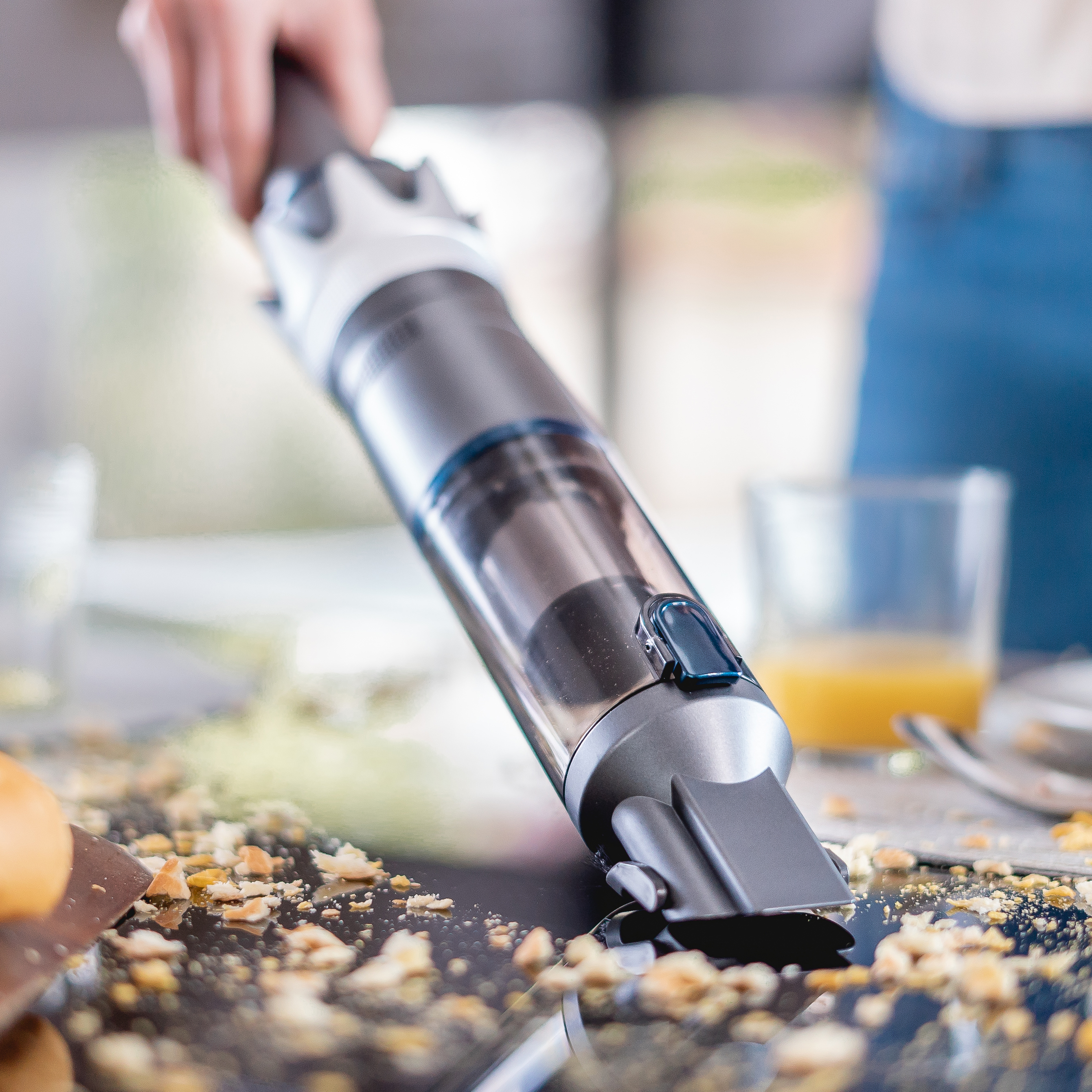 Ein Staubsauger reinigt einen Tisch. Krümel und Ablagerungen sind auf der Tischoberfläche.
