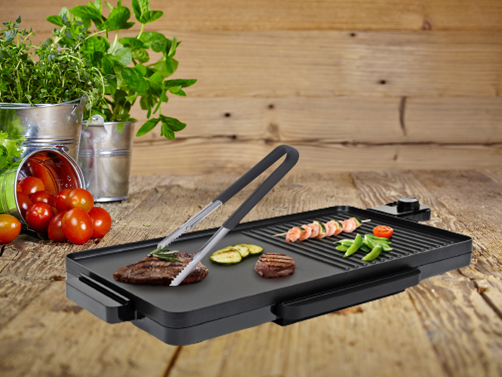 Elektrischer Grill mit Essen, Zange und Pflanzen im Hintergrund.