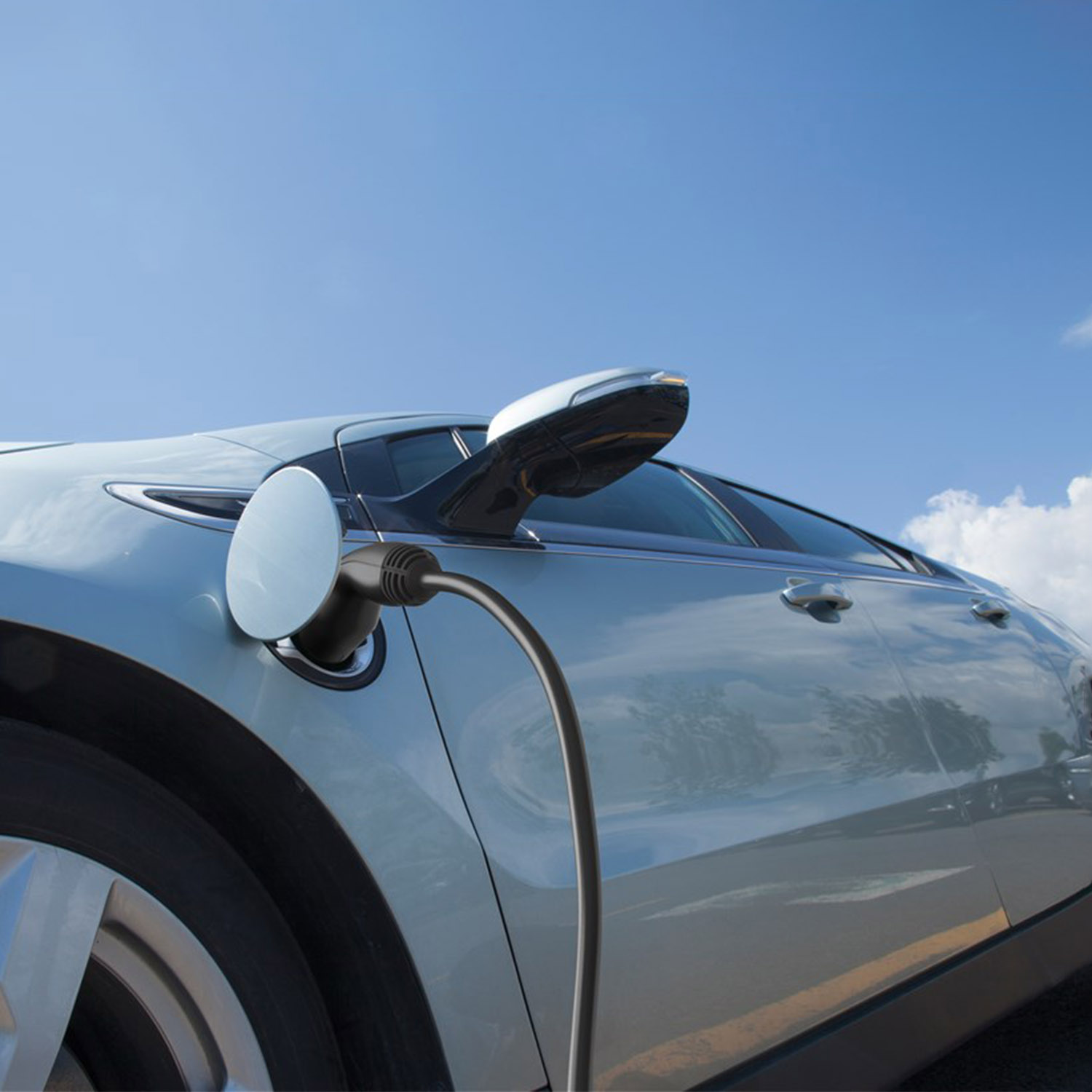 Ein silbernes Elektroauto, das mit einem schwarzen Kabel unter blauem Himmel mit Wolken geladen wird.