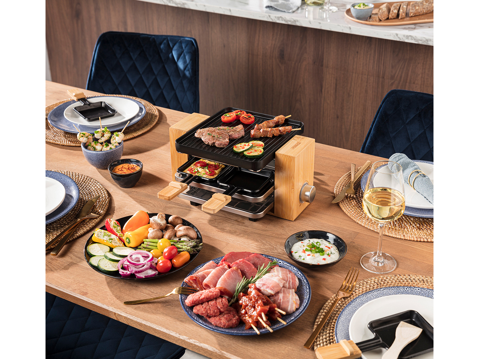 Drewniany stół z grillem do raclette, składnikami, talerzami i kieliszkami do wina.