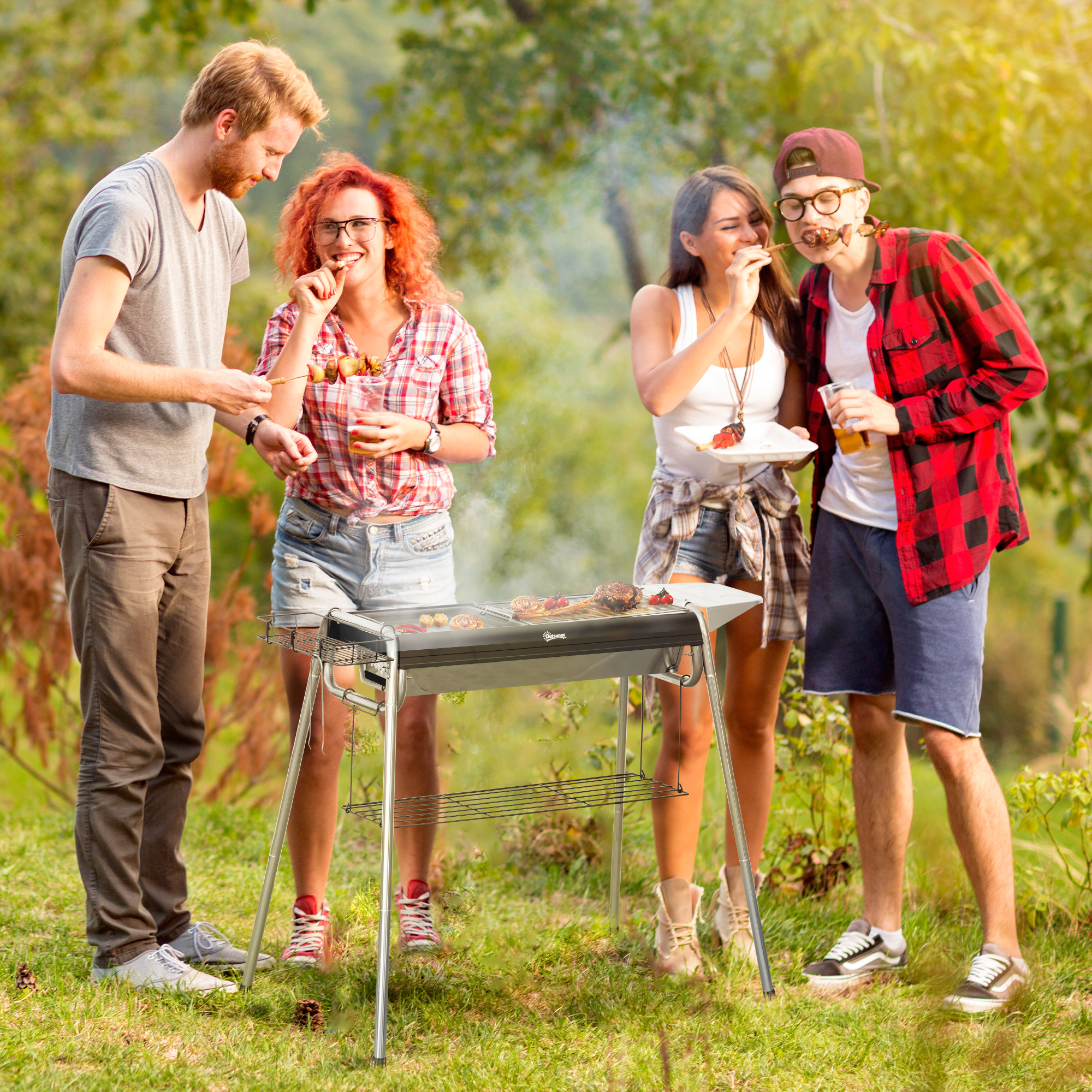 Quattro persone attorno a un barbecue che cucinano all'aperto. Sorridono e si divertono. Sfondo erboso.