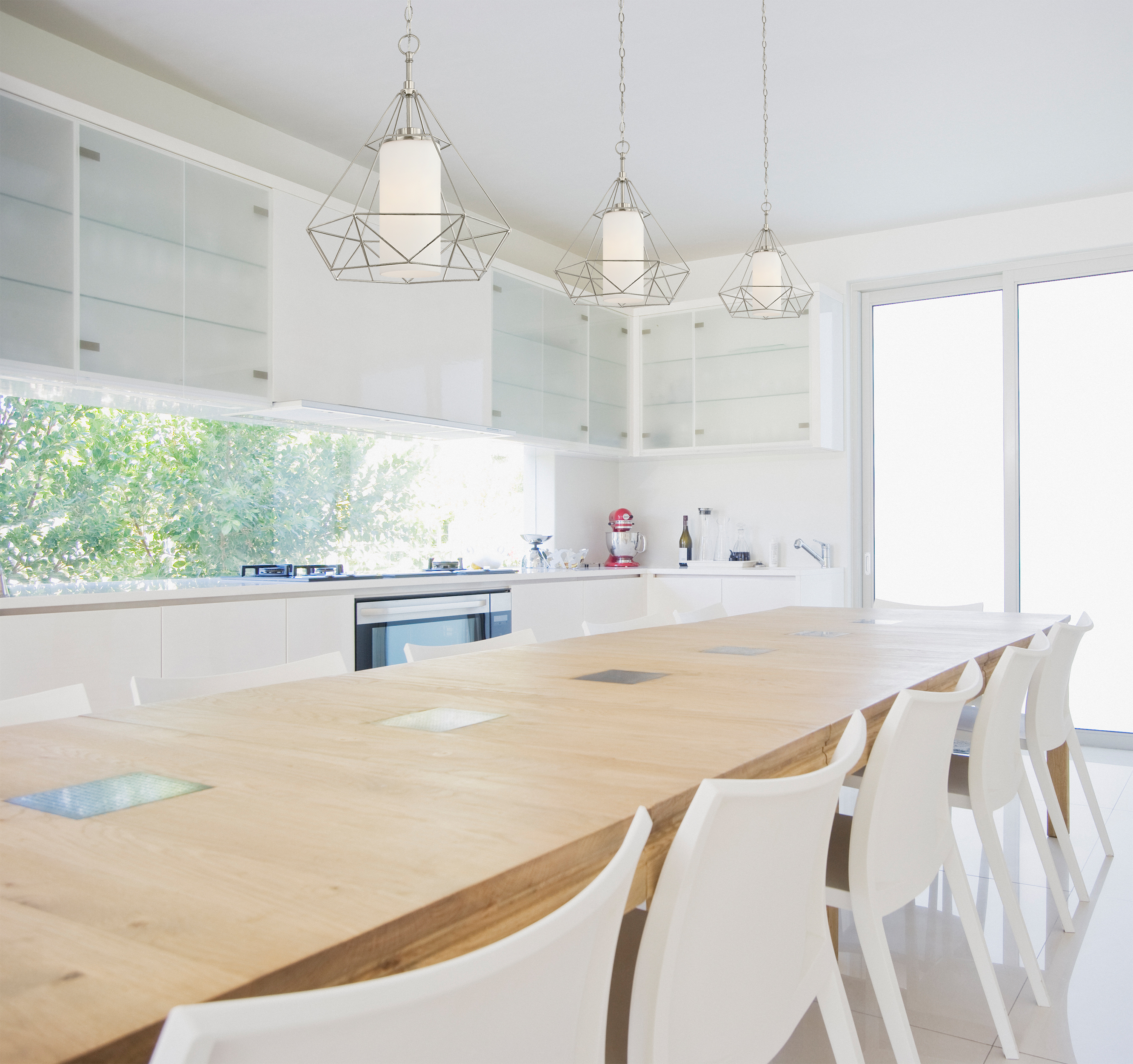 Moderne Küche mit langem Holztisch und weißen Stühlen. Deckenleuchten und weiße Schränke.