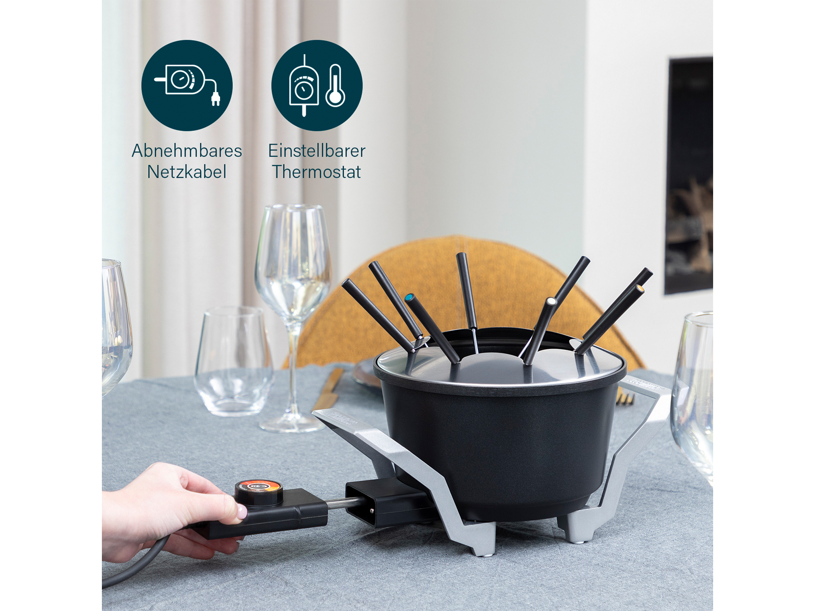 Garnek do fondue na stole z przewodem zasilającym i panelem sterowania. Widoczna dłoń.