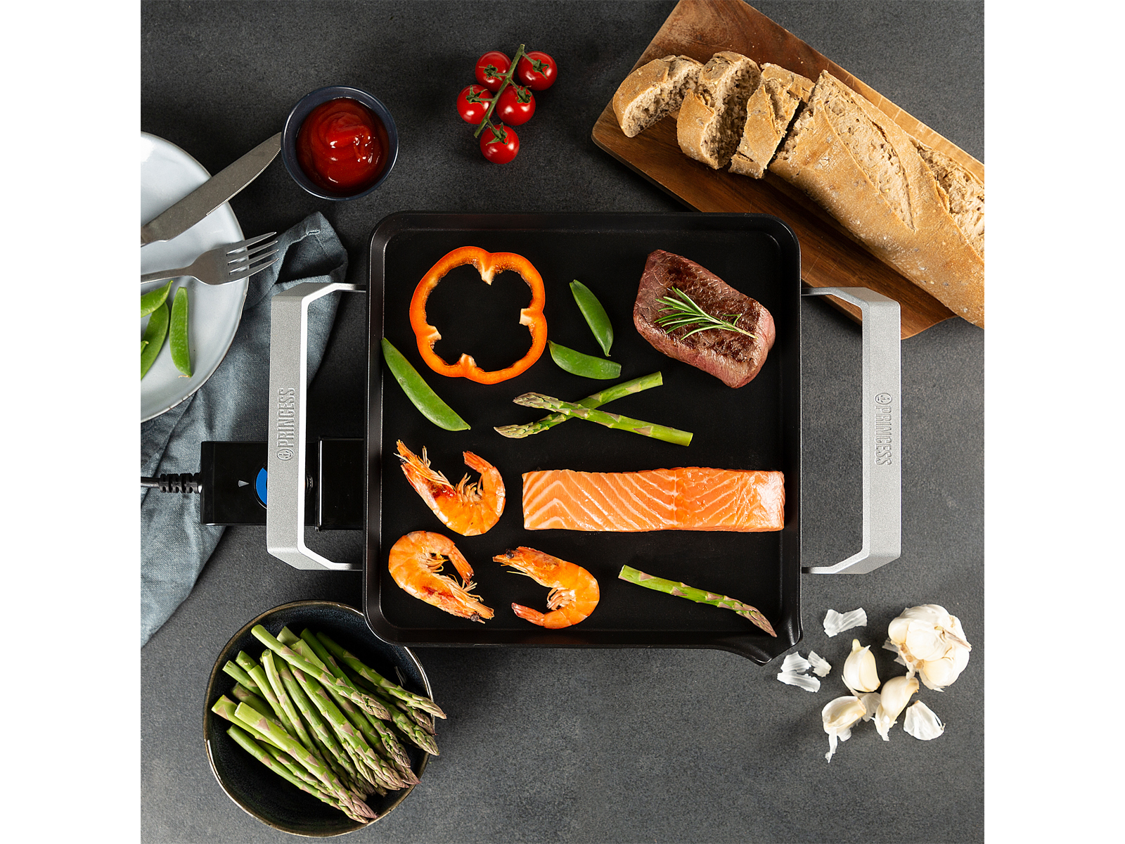 Una parrilla con comida: verduras, camarones, salmón y carne. Plato y pan junto a ella.