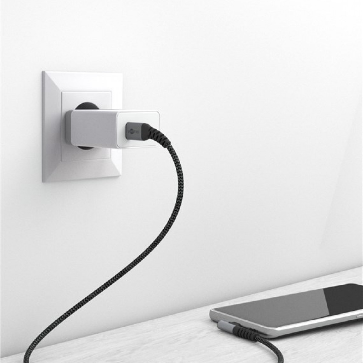 A white wall outlet with a silver charger and a black cable connected to a phone.
