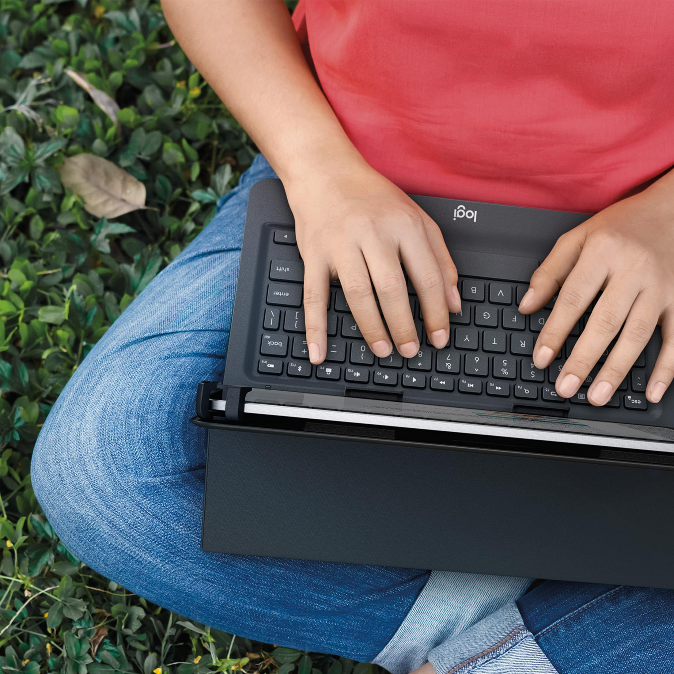 Person tippt auf einer schwarzen Tastatur, Schoß sitzt im grünen Gras.