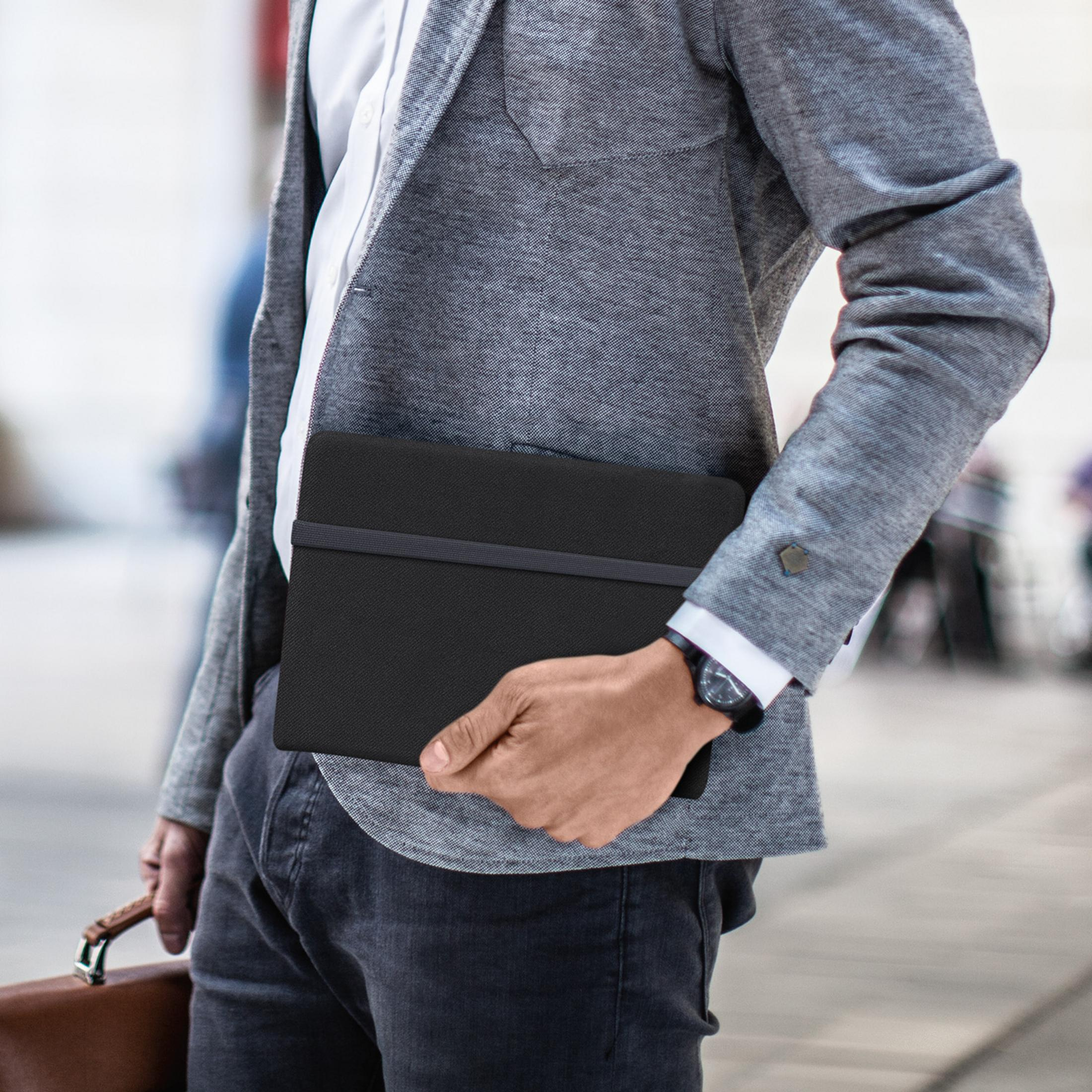 Ein Mann hält ein schwarzes Notizbuch in seiner linken Hand, trägt einen grauen Blazer und Jeans.
