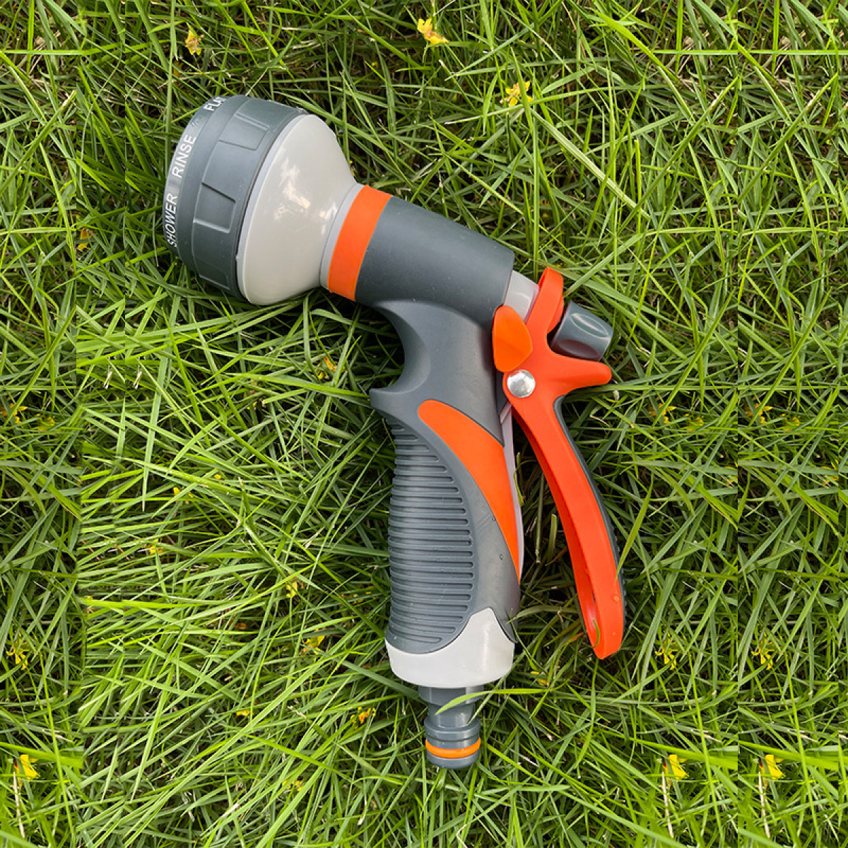 Eine grau-orange Gartenschlauchdüse auf grünem Gras. Hat Dusch-, Spül- und Impulseinstellungen.