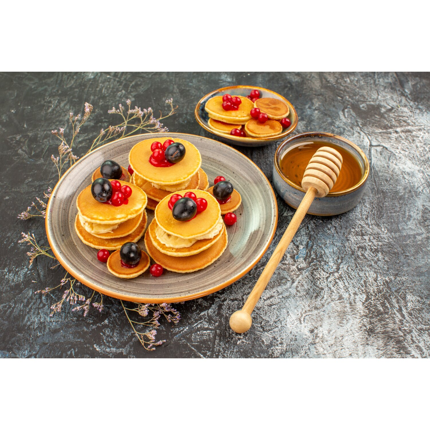 Pfannkuchen mit Beeren und Honig, serviert auf einem Teller mit einem Honigdipper. Mehr Pfannkuchen und Honig.