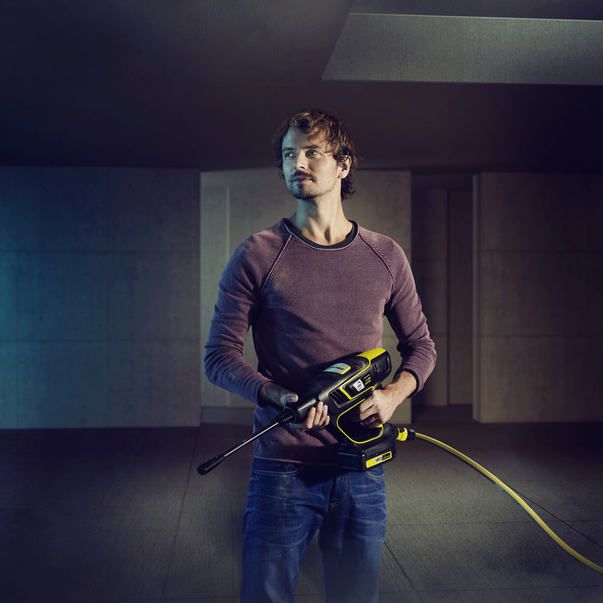 Man holding a black and yellow pressure washer in an industrial setting.
