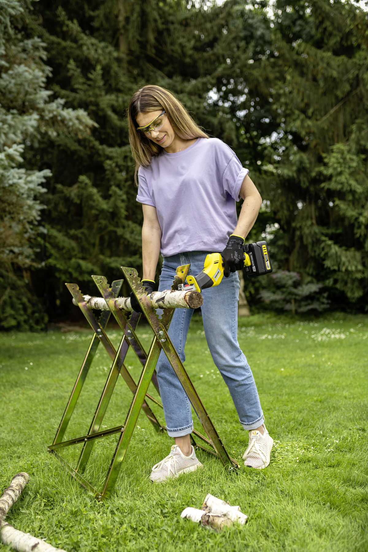 Frau schneidet Holz mit Akku-Säbelsäge, trägt Schutzbrille und Handschuhe.