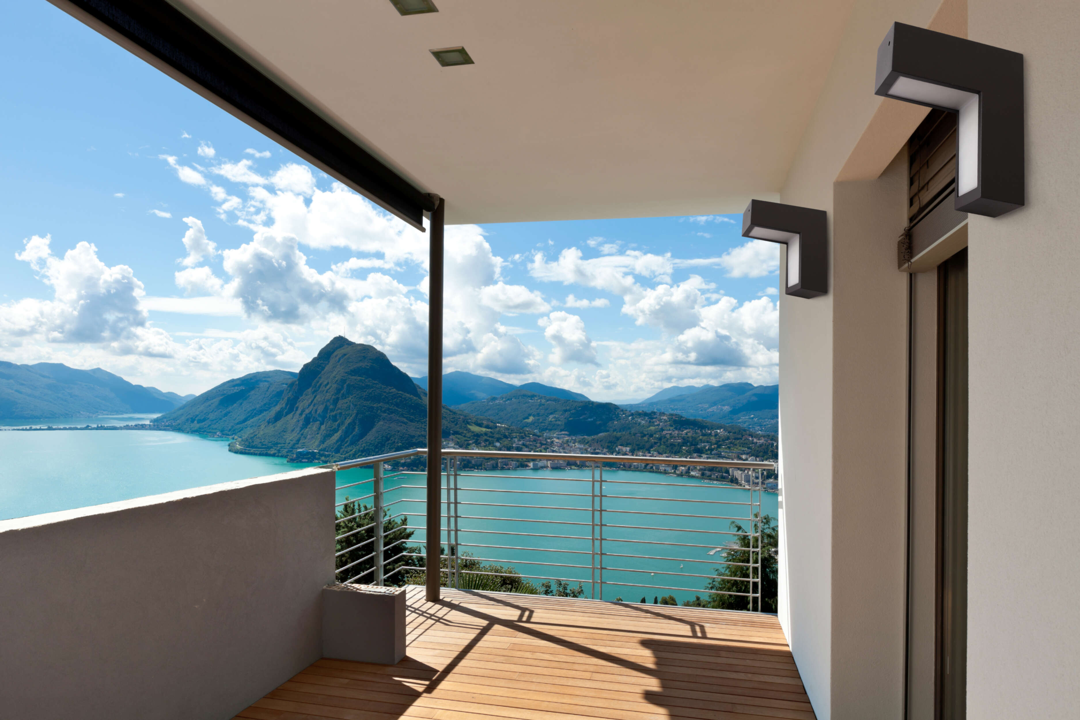 Ein Balkon mit Blick auf einen See und Berge, mit hellem blauem Himmel und Wolken.