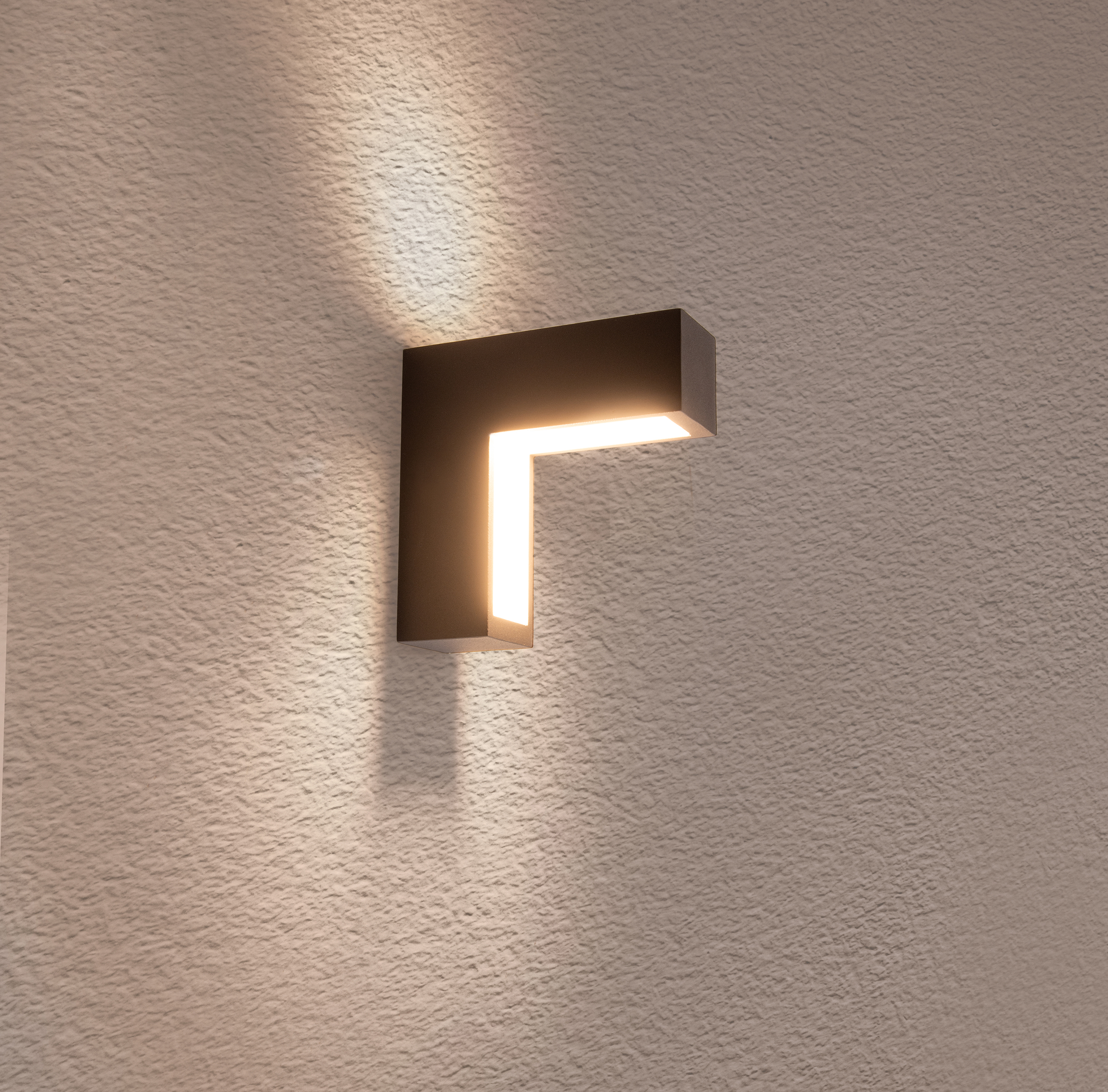 Schwarze L-förmige Wandleuchte mit warmem Licht, an strukturierter Wand.