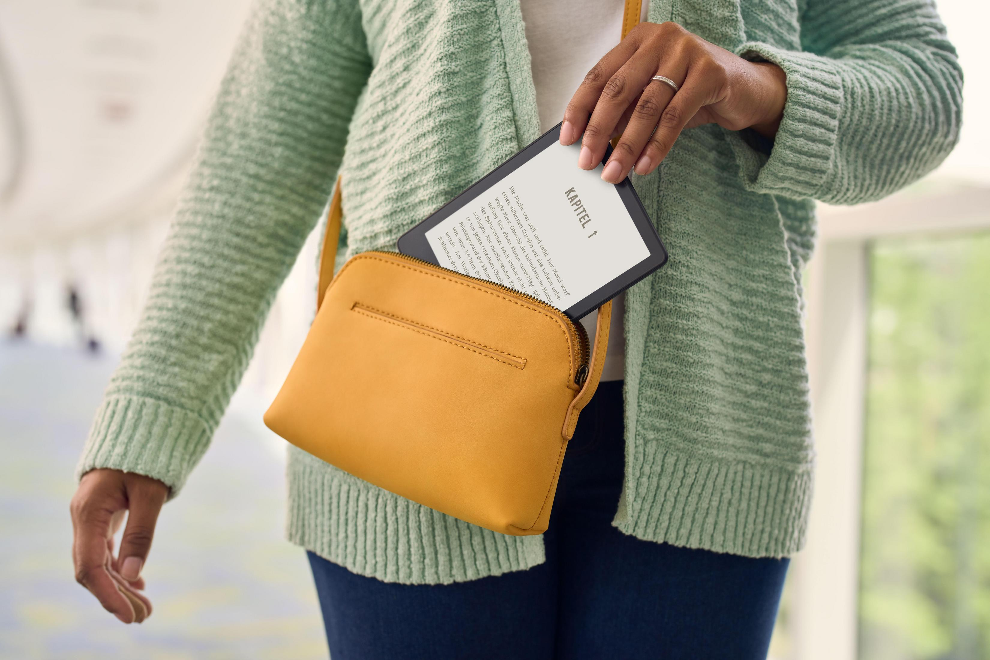 Frau mit gelber Tasche, hält E-Reader, liest Seite 1, in einem Flur.
