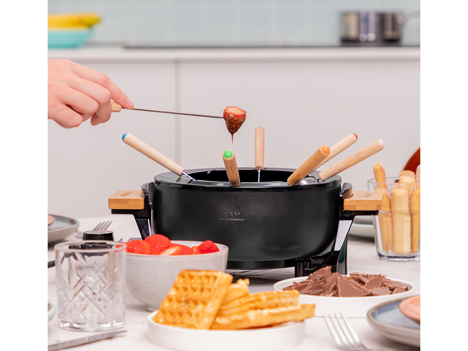 Una olla de fondue con varios elementos para mojar: fresas, gofres y chocolate.