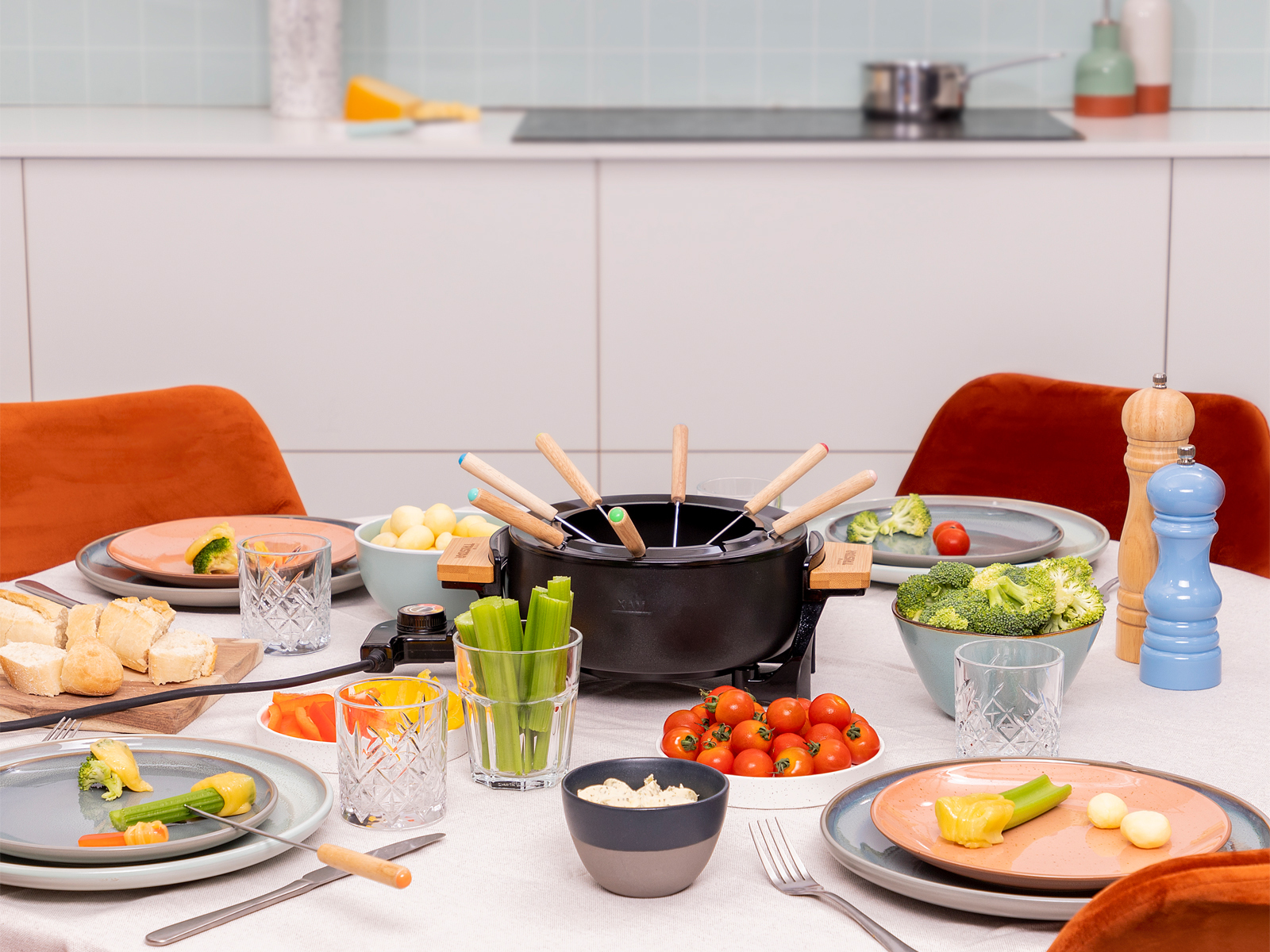 Juego de fondue en una mesa con comida y sillas. Olla de fondue negra con tenedores, platos de verduras.