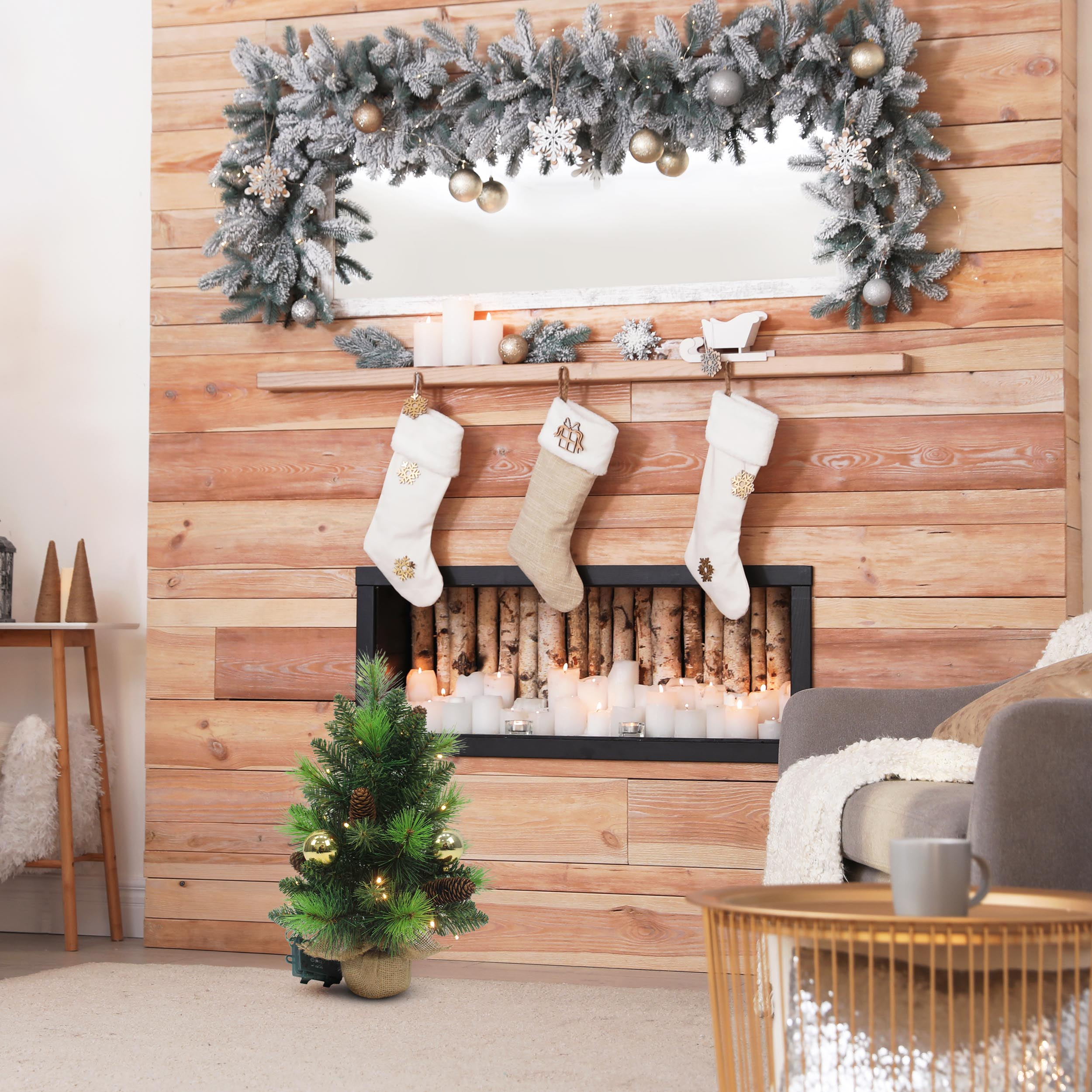 Eine festliche Kaminszene mit Strümpfen, einem kleinen Weihnachtsbaum und einem Spiegel mit Girlande.
