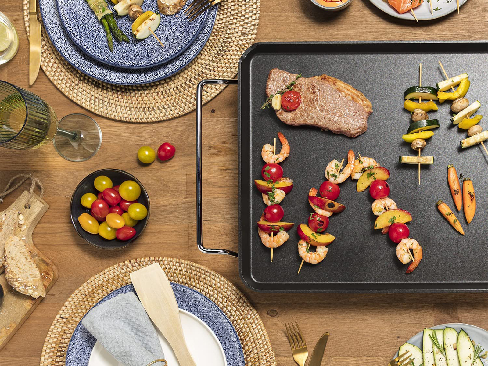 Ein Grill mit gekochtem Essen, darunter Garnelenspieße, Fleisch und Gemüse. Holztisch.