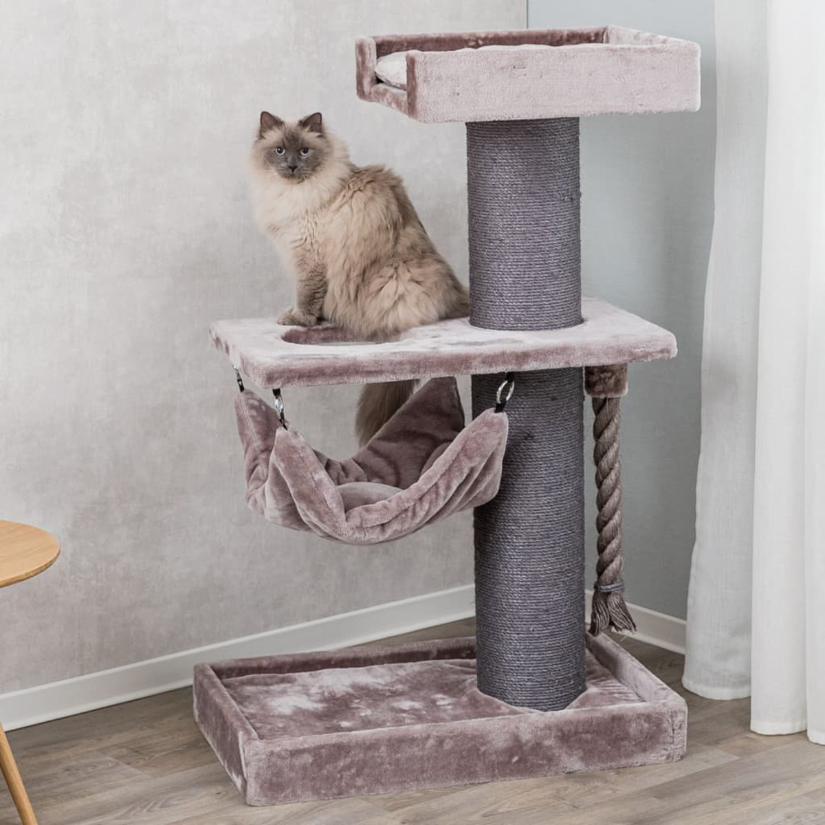 Un gato se sienta en un árbol para gatos, con una hamaca y un poste rascador, dentro de una habitación.