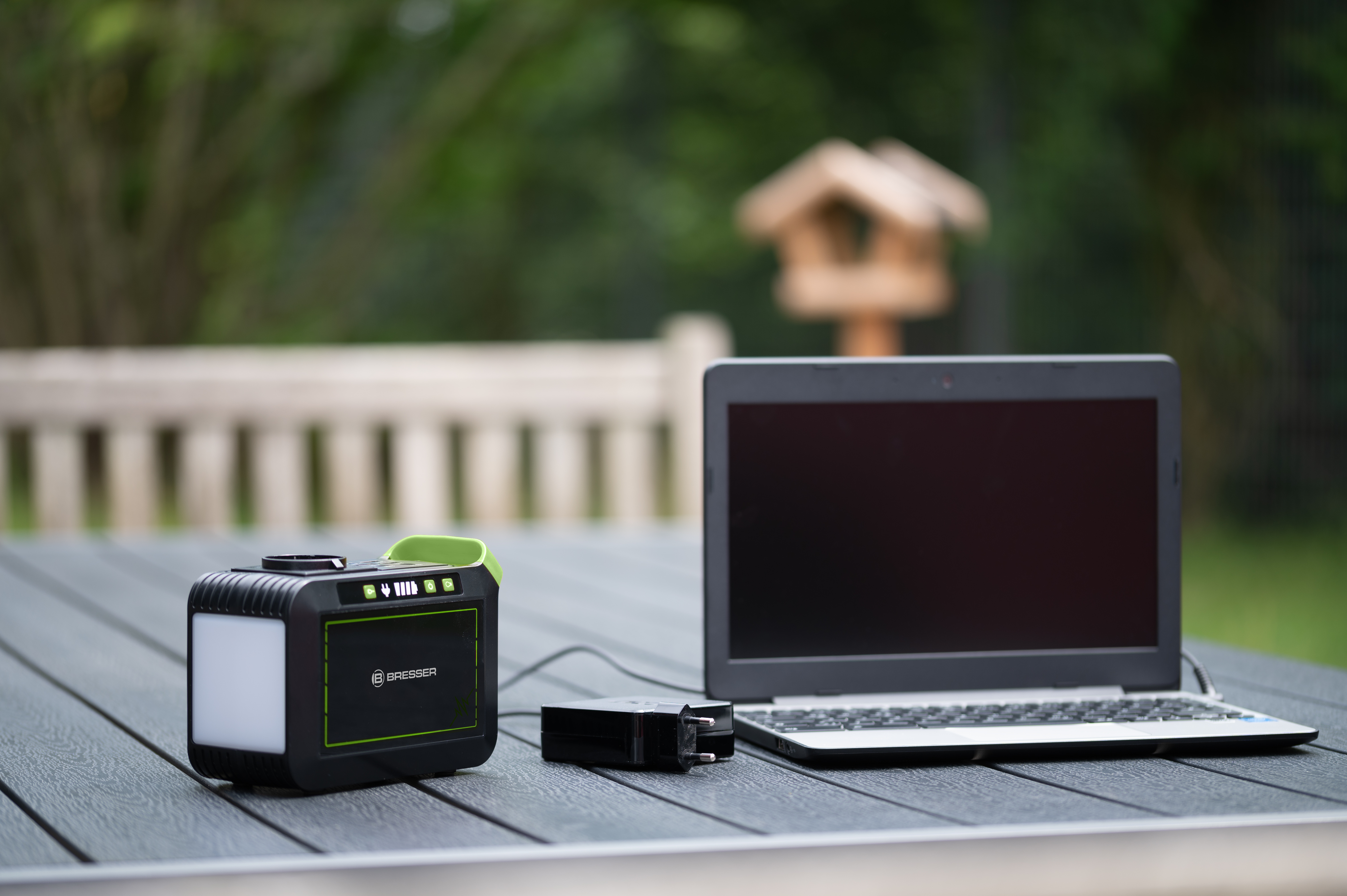 Una estación de energía portátil, una computadora portátil y un cargador en una mesa de madera al aire libre.
