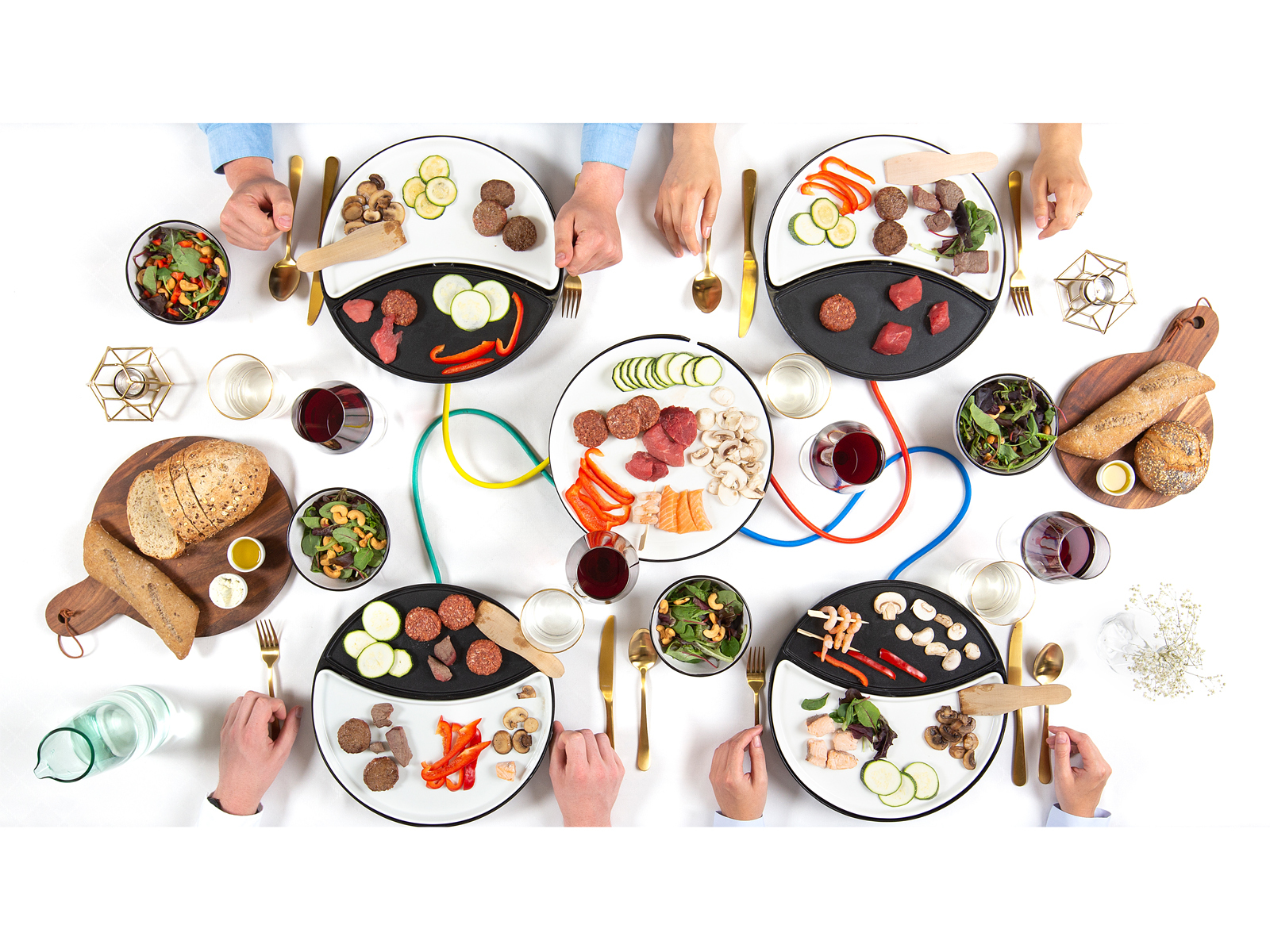 Kilka osób wokół stołu, jedzących różne potrawy na indywidualnych talerzach, widok z góry.