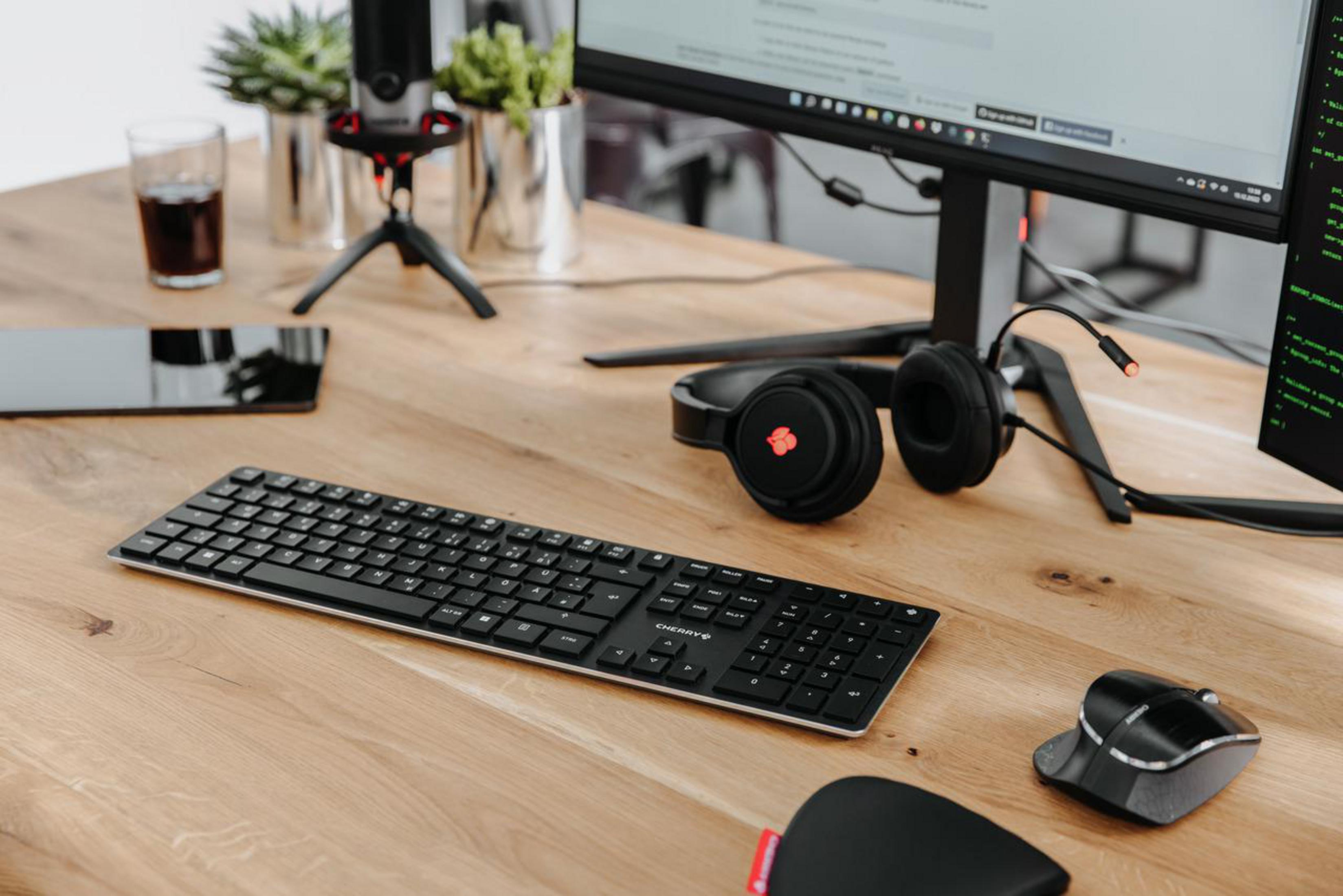 Konfiguracja biurka z klawiaturą, myszą, słuchawkami i monitorem. Są rośliny i szklanka.