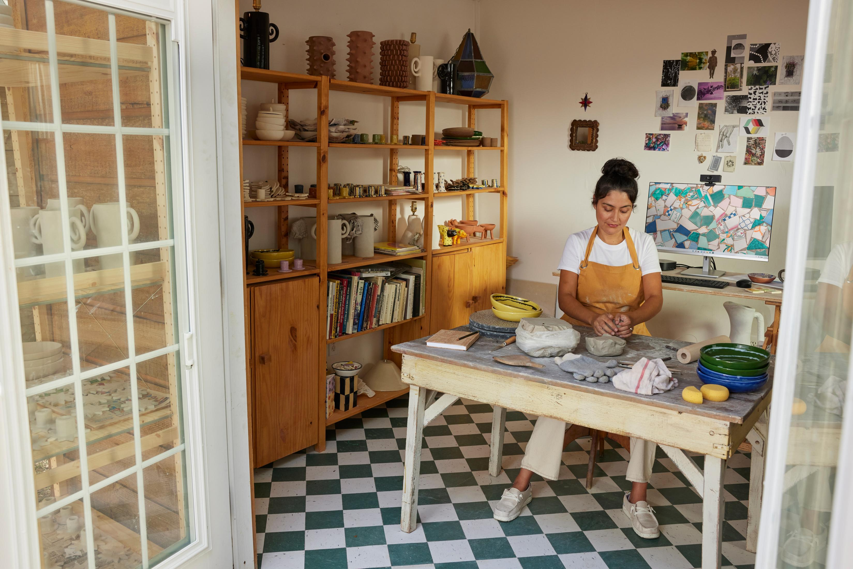 Kobieta w studio, robiąca ceramikę. Półki z ceramiką, szachownica i światło słoneczne.