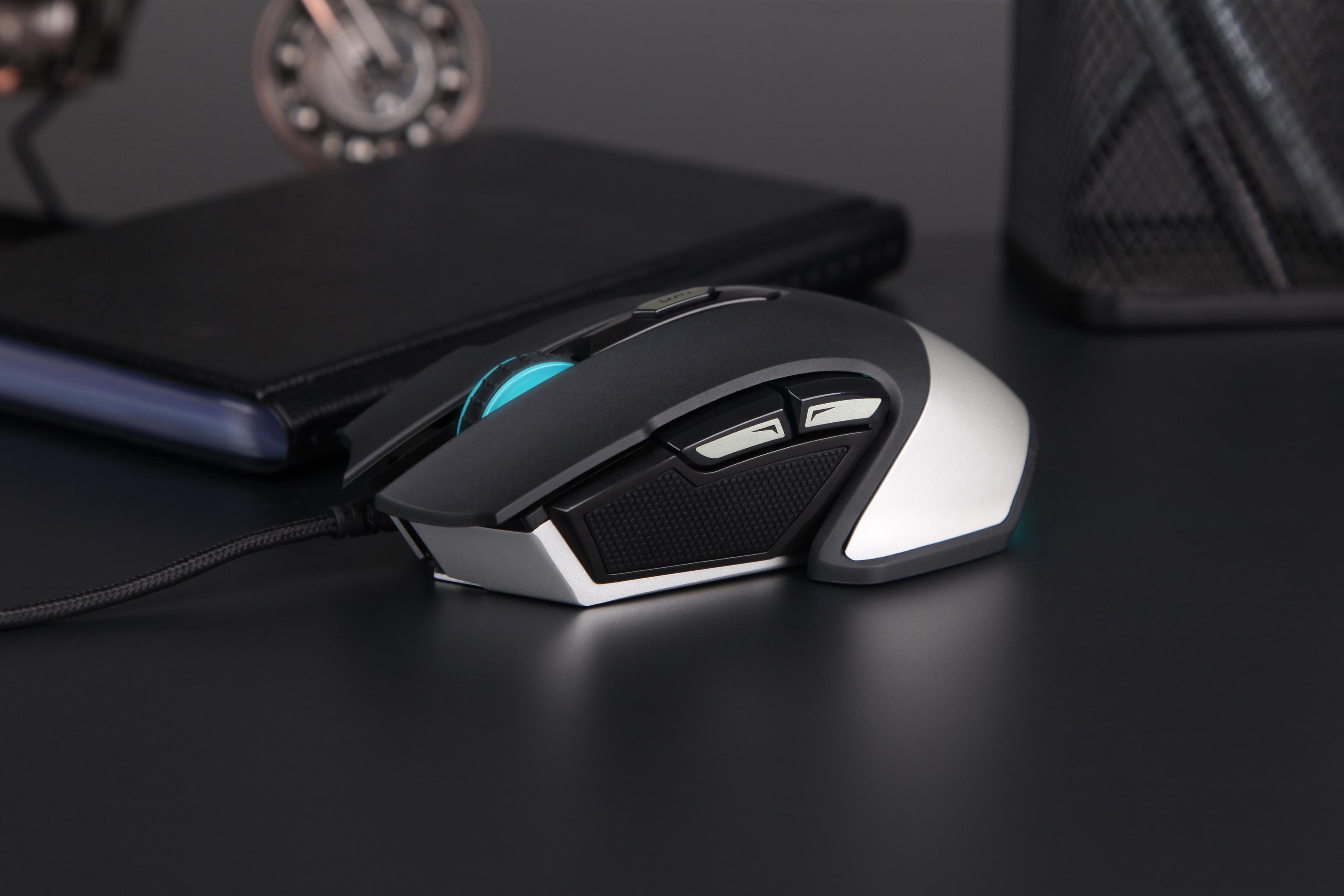 Czarna i srebrna mysz gamingowa na czarnym biurku. Przyciski i kółko przewijania z niebieskim światłem.
